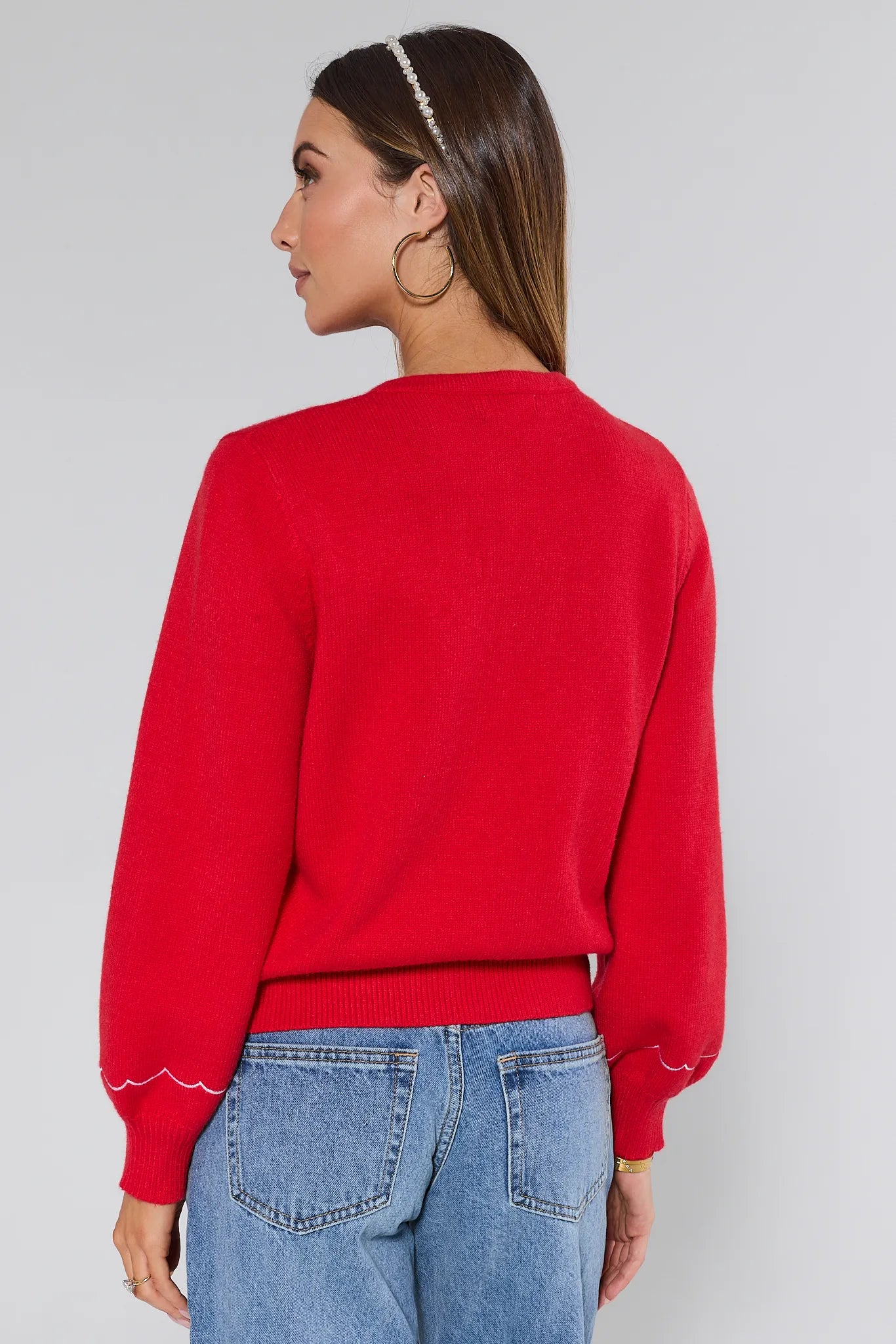 Woman wearing a red embroidered Ginger cardigan over a white top and blue jeans on a plain background