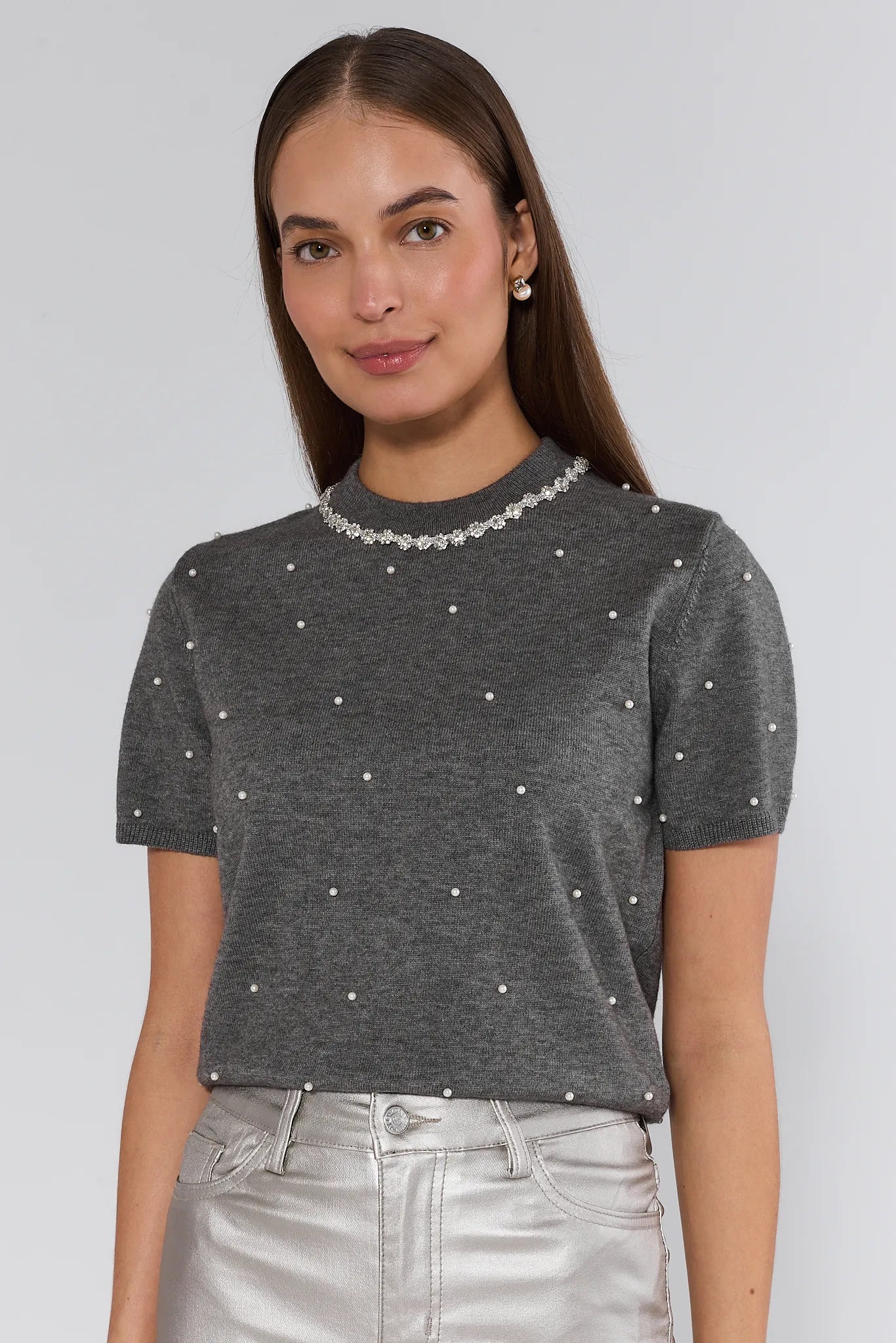 Woman wearing a gray short-sleeve top with pearl embellishments on a plain background