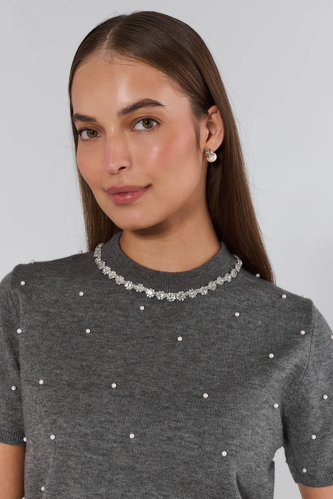 Woman wearing a gray sweater with pearl embellishments on a plain background