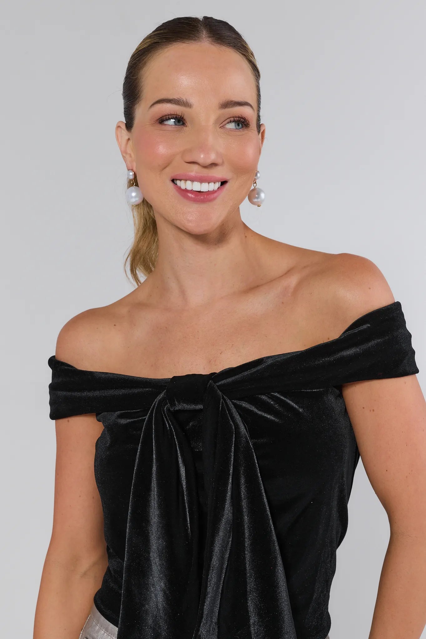 Woman wearing a black off-shoulder velvet dress against a plain background