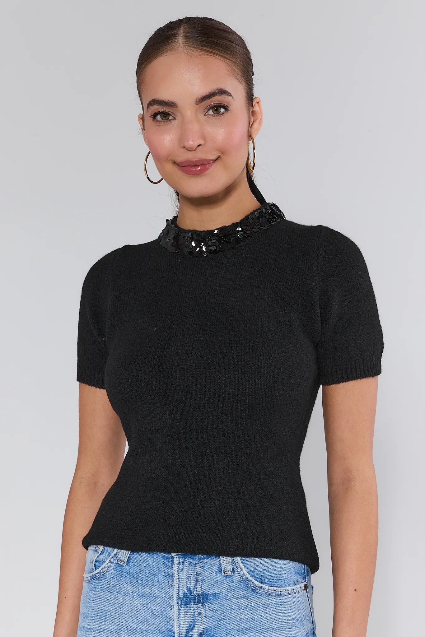 Woman wearing a black short-sleeve Vicki Sweater with a sequin collar against a white background