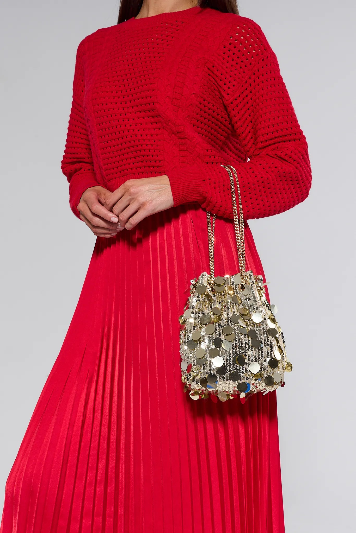 Person wearing a red outfit with a sparkling handbag on a plain background