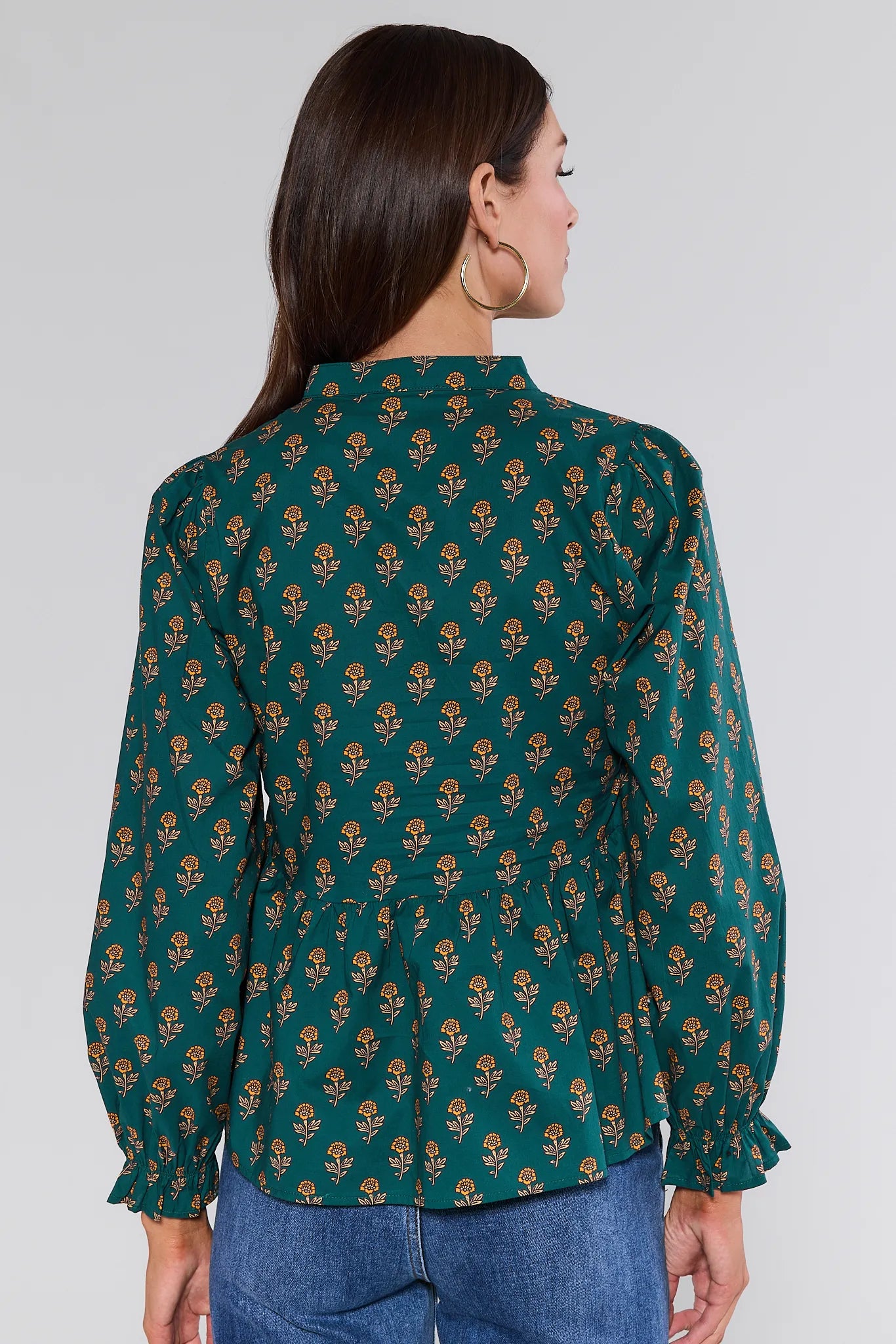 Woman wearing a green patterned Fallon Top with blue jeans on a white background