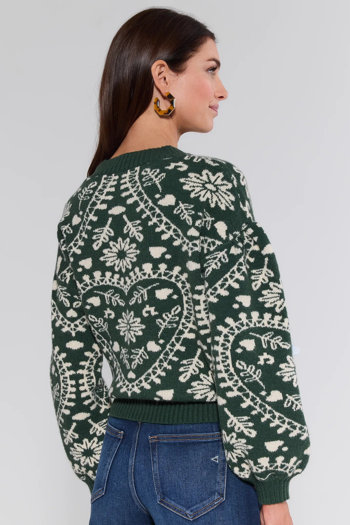Woman wearing a green Pamela Sweater with white floral patterns on a plain background