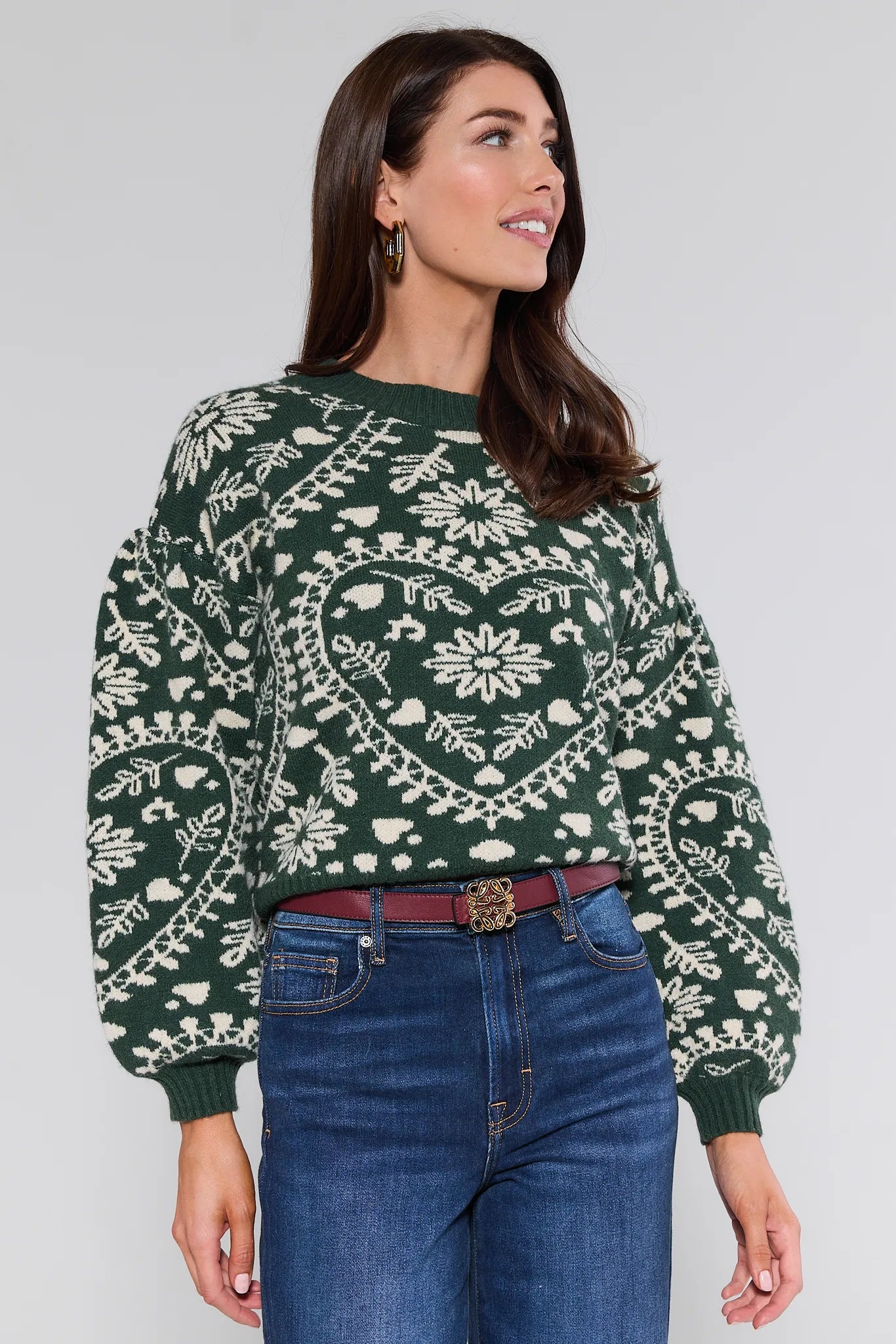 Woman wearing a green patterned Pamela Sweater and blue jeans against a plain background