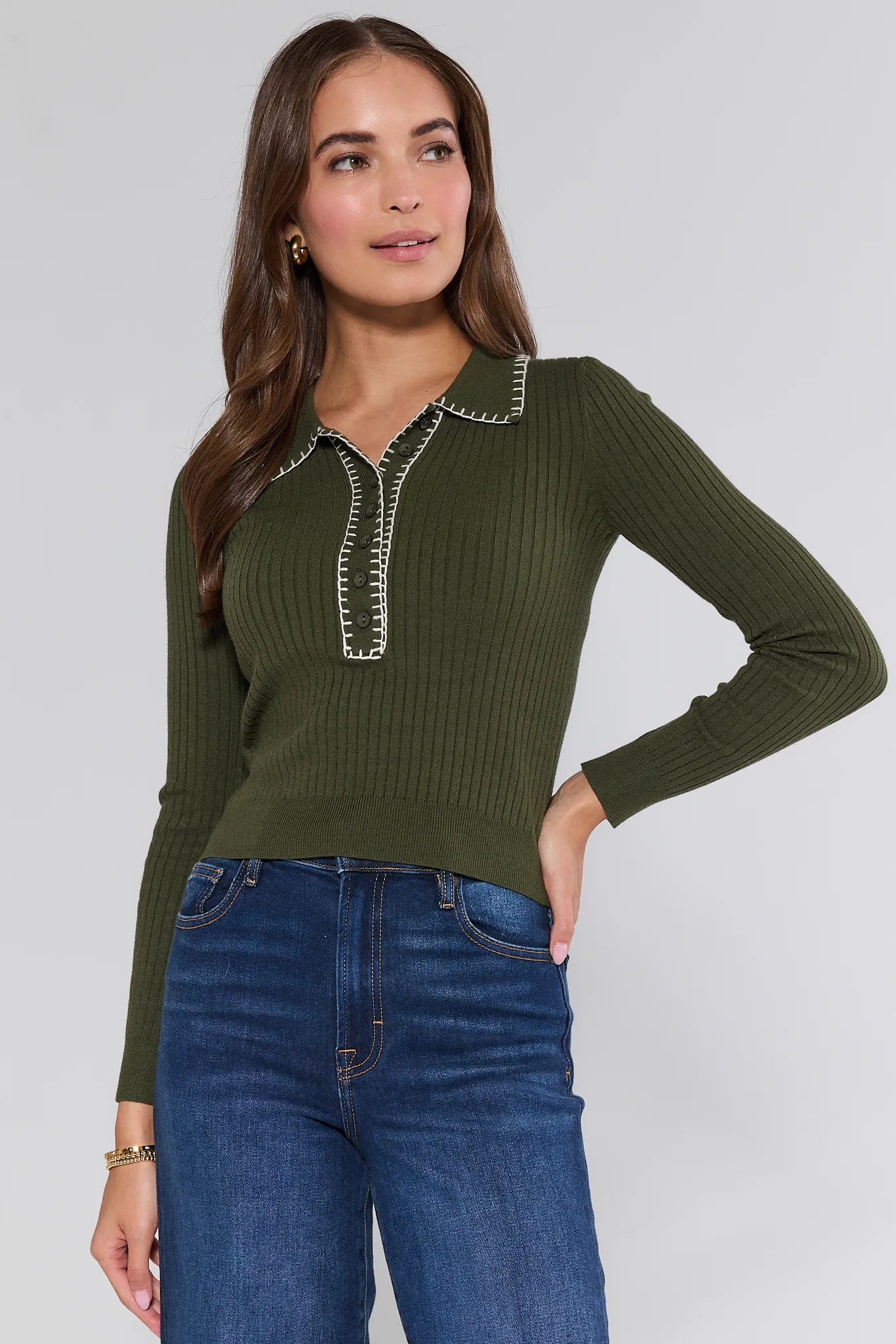 Woman wearing a green ribbed Shayla Sweater with decorative buttons and blue jeans on a white background