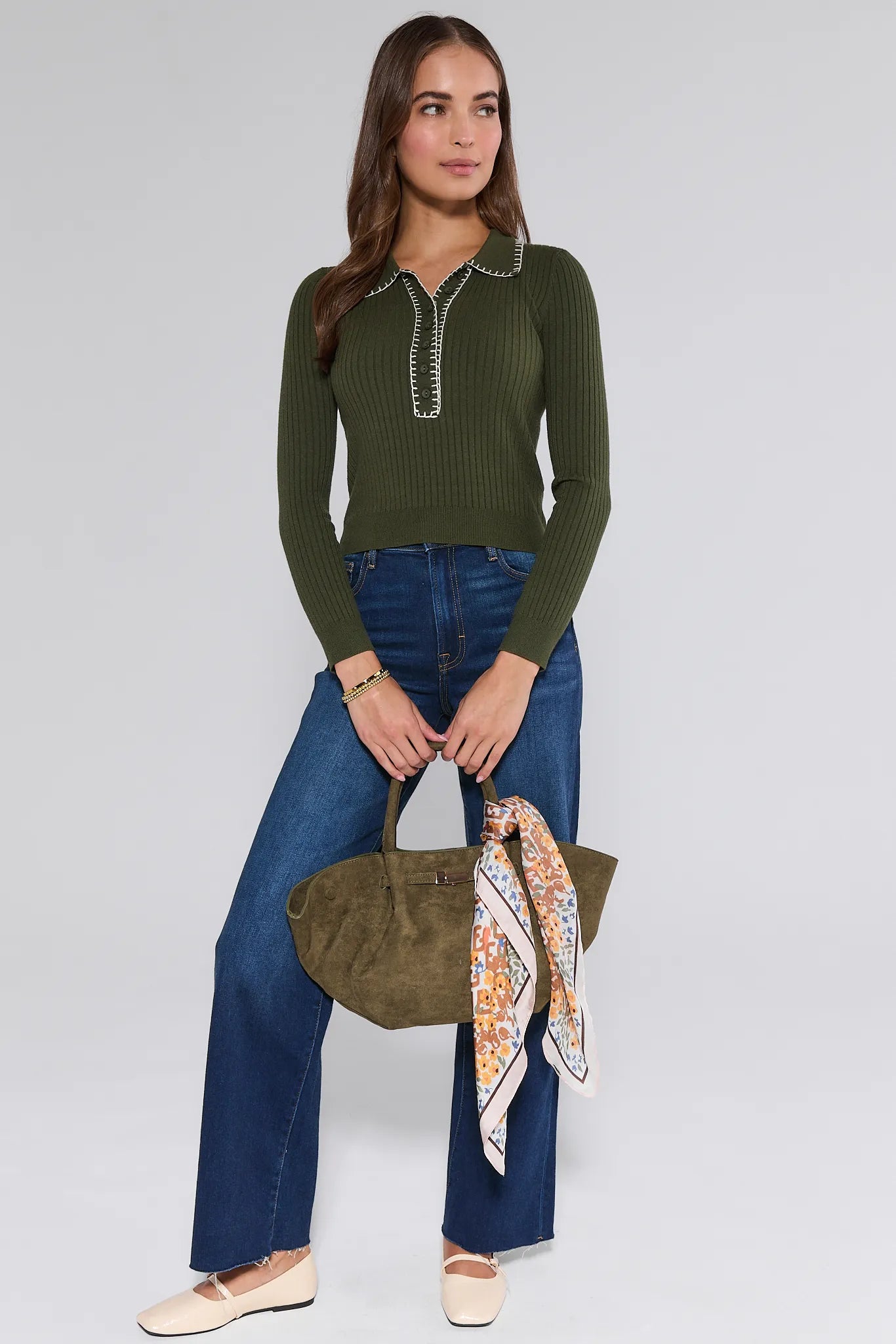 Woman wearing a green long-sleeve Shayla Sweater and blue jeans, holding a green handbag with a colorful scarf.