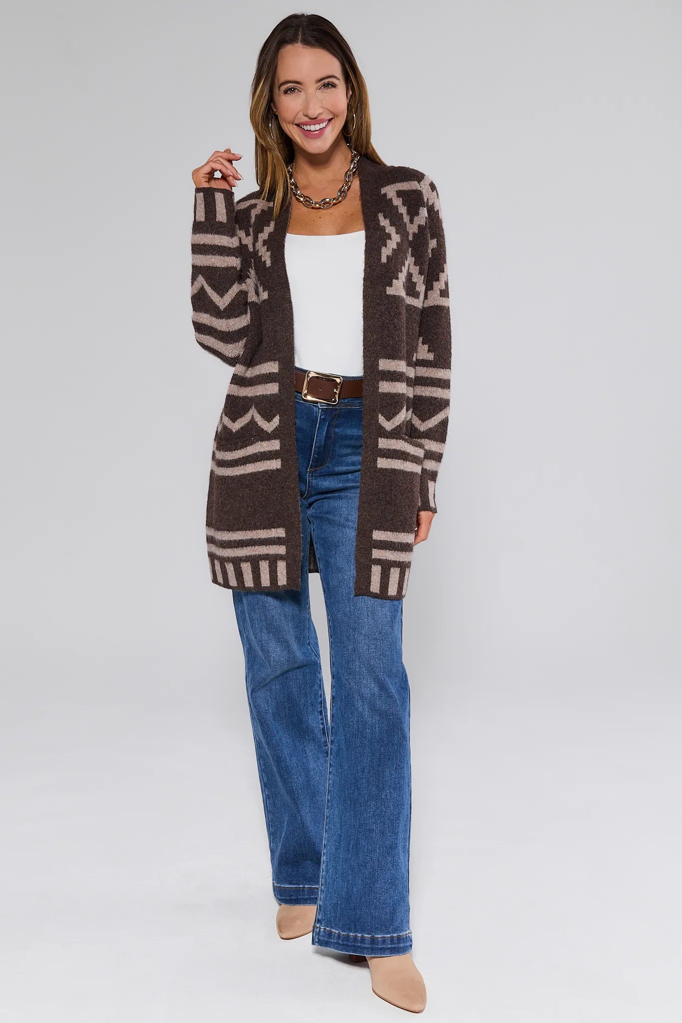 Woman wearing a patterned Helena Cardigan Brown, white top, and blue jeans on a white background