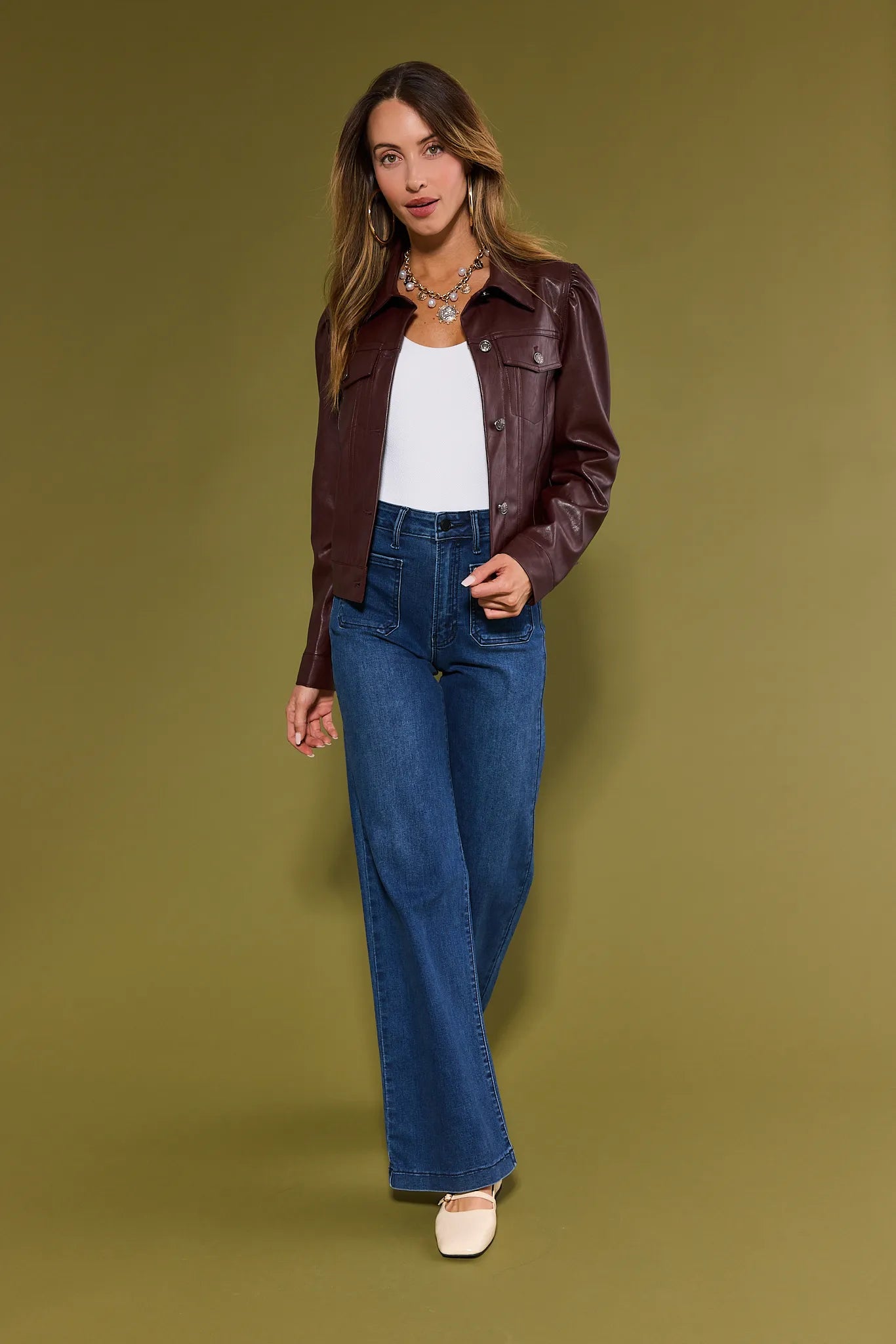Woman wearing a brown Roxanna Leather Jacket and blue jeans on a green background