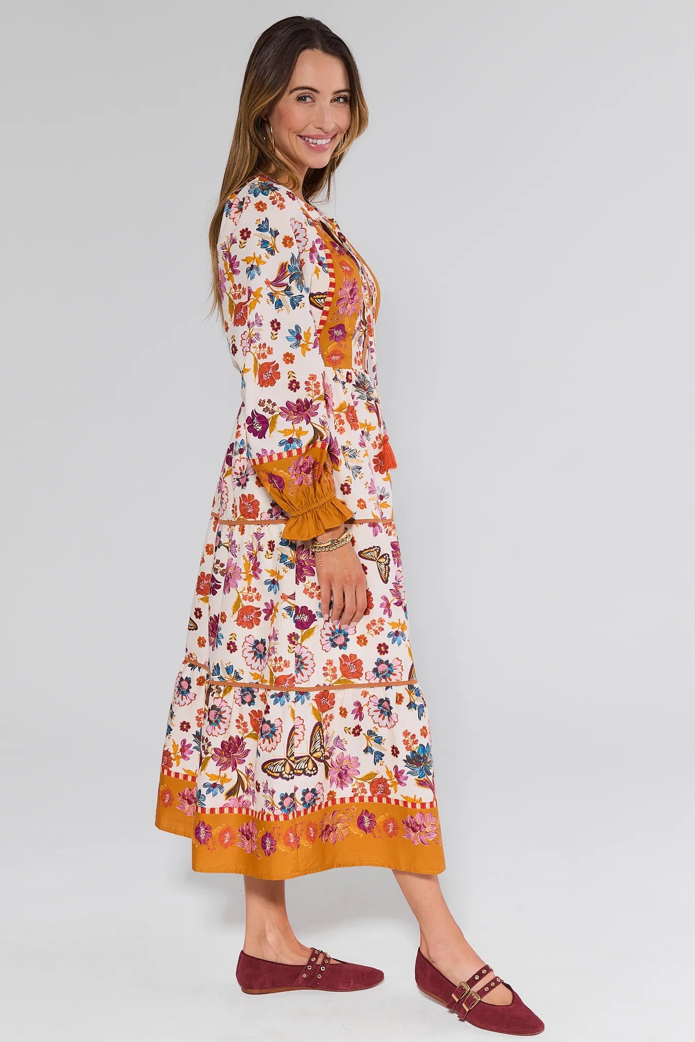 Woman wearing a floral Shiloh Dress with orange accents on a white background