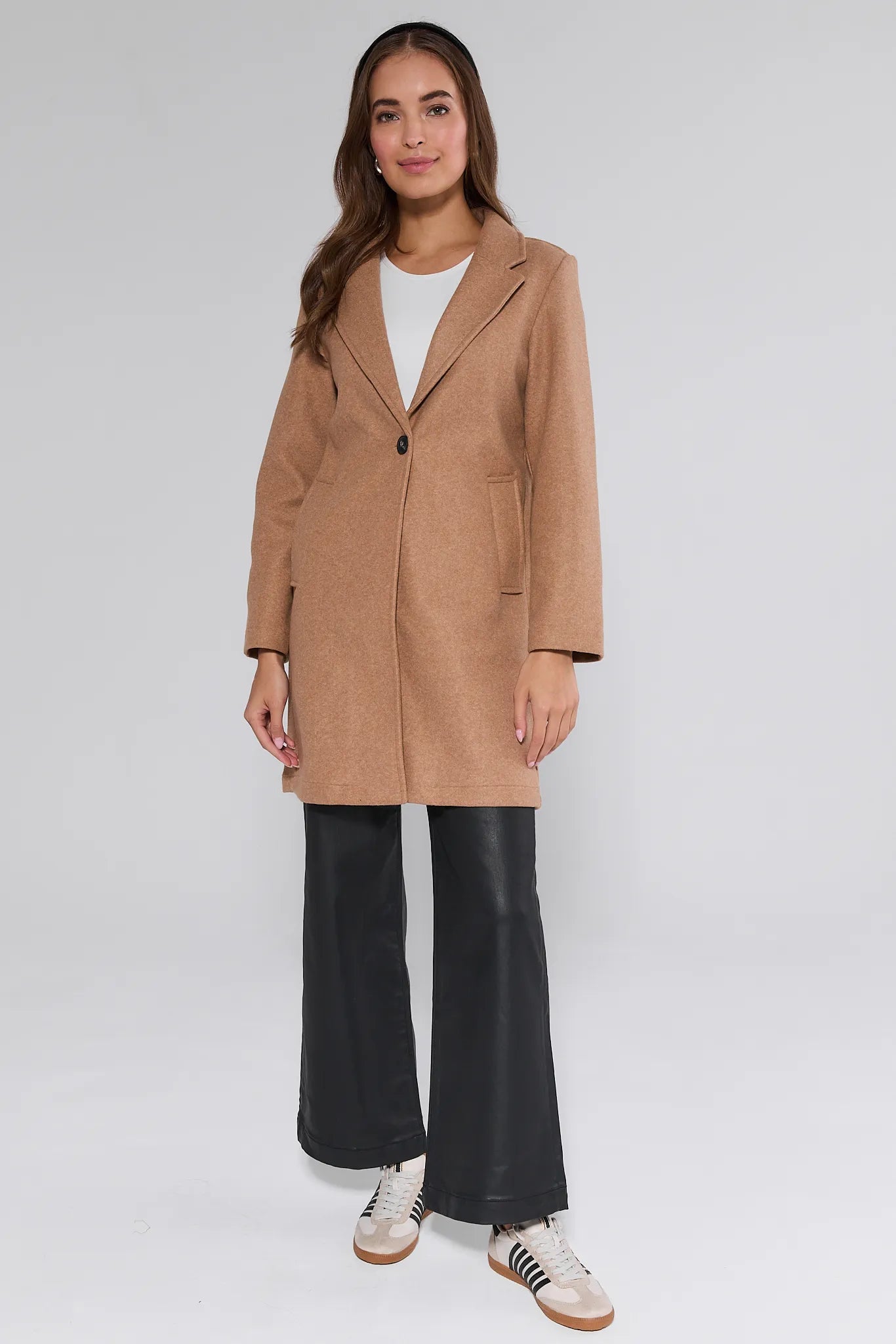 Woman wearing a beige Lauren Coat with black pants and white sneakers on a plain background