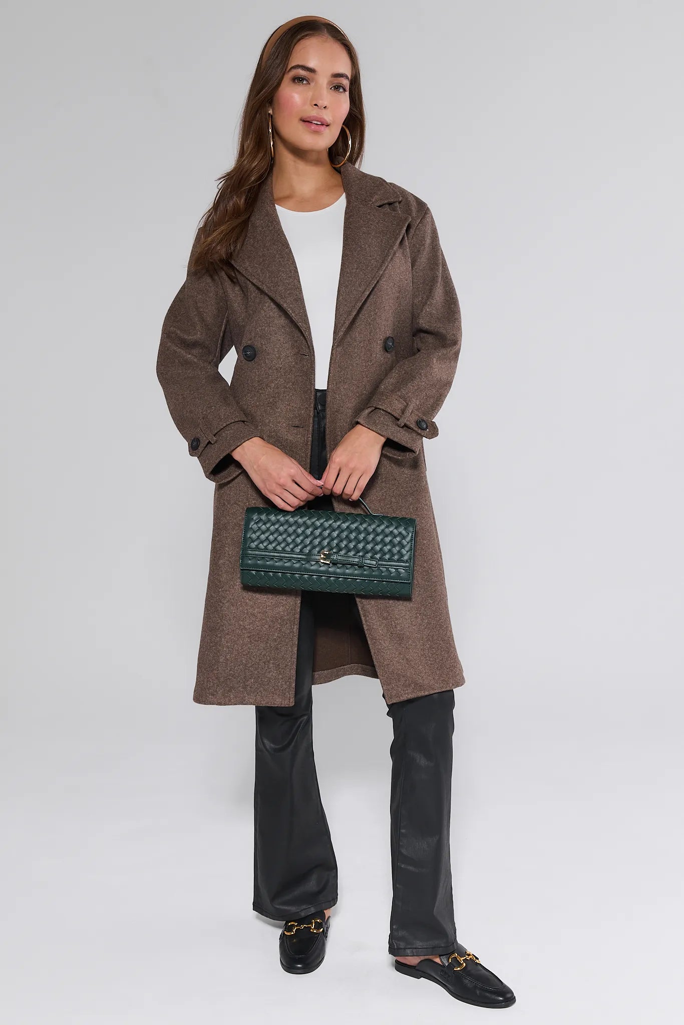 Woman wearing a brown Sadie Coat holding a green handbag on a white background