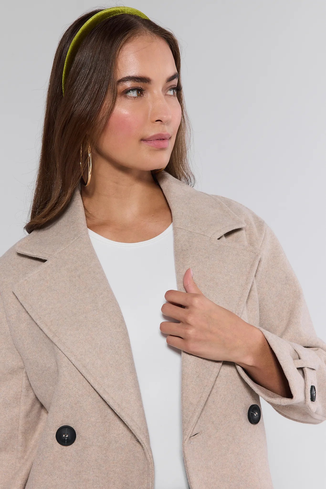 Woman wearing a beige Sadie Coat over a white top against a plain background