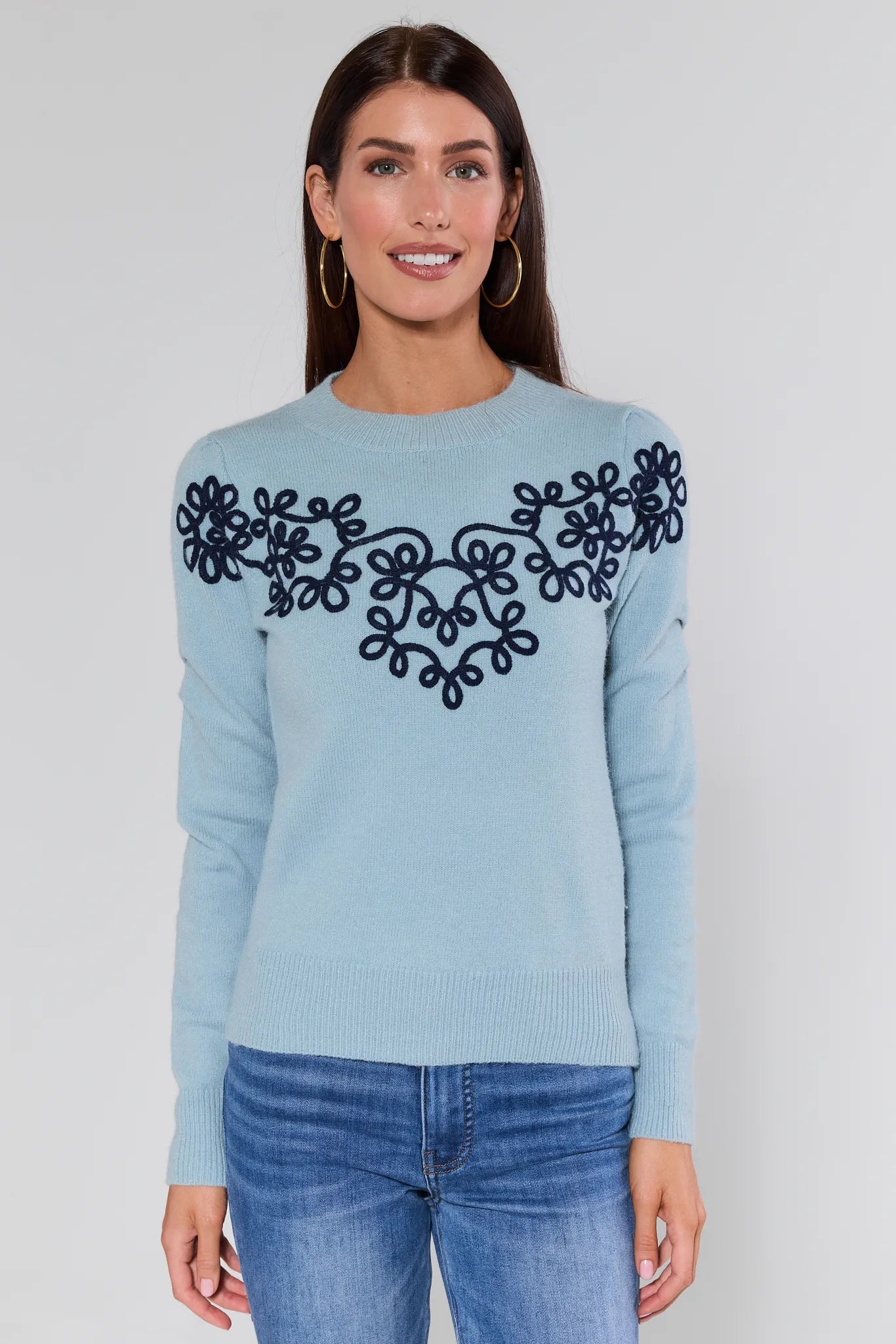 Woman wearing a Natasha Blue Embroidered Sweater with black embroidery on a plain background