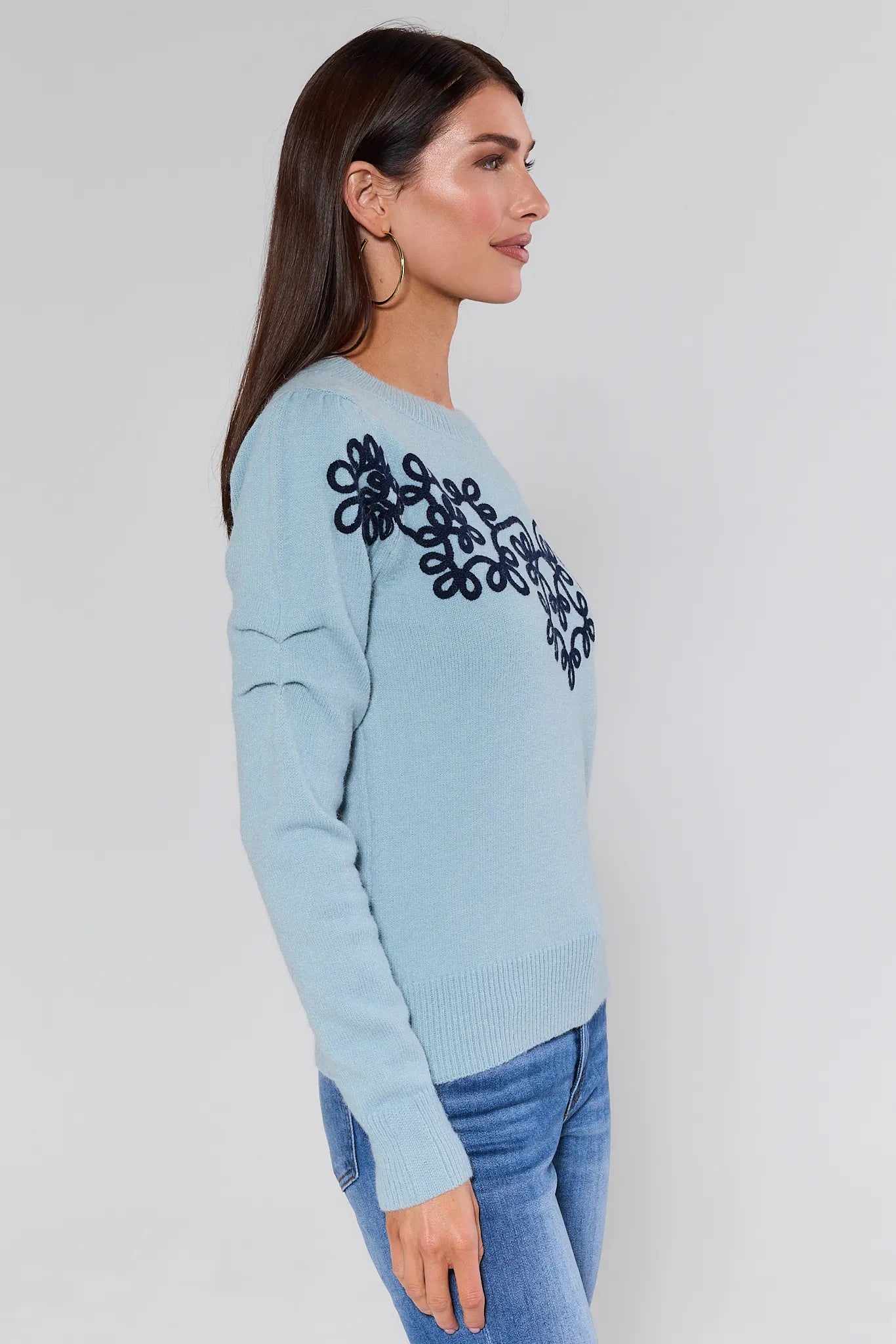 Woman wearing a Natasha Blue Embroidered Sweater with black embroidery on a plain background