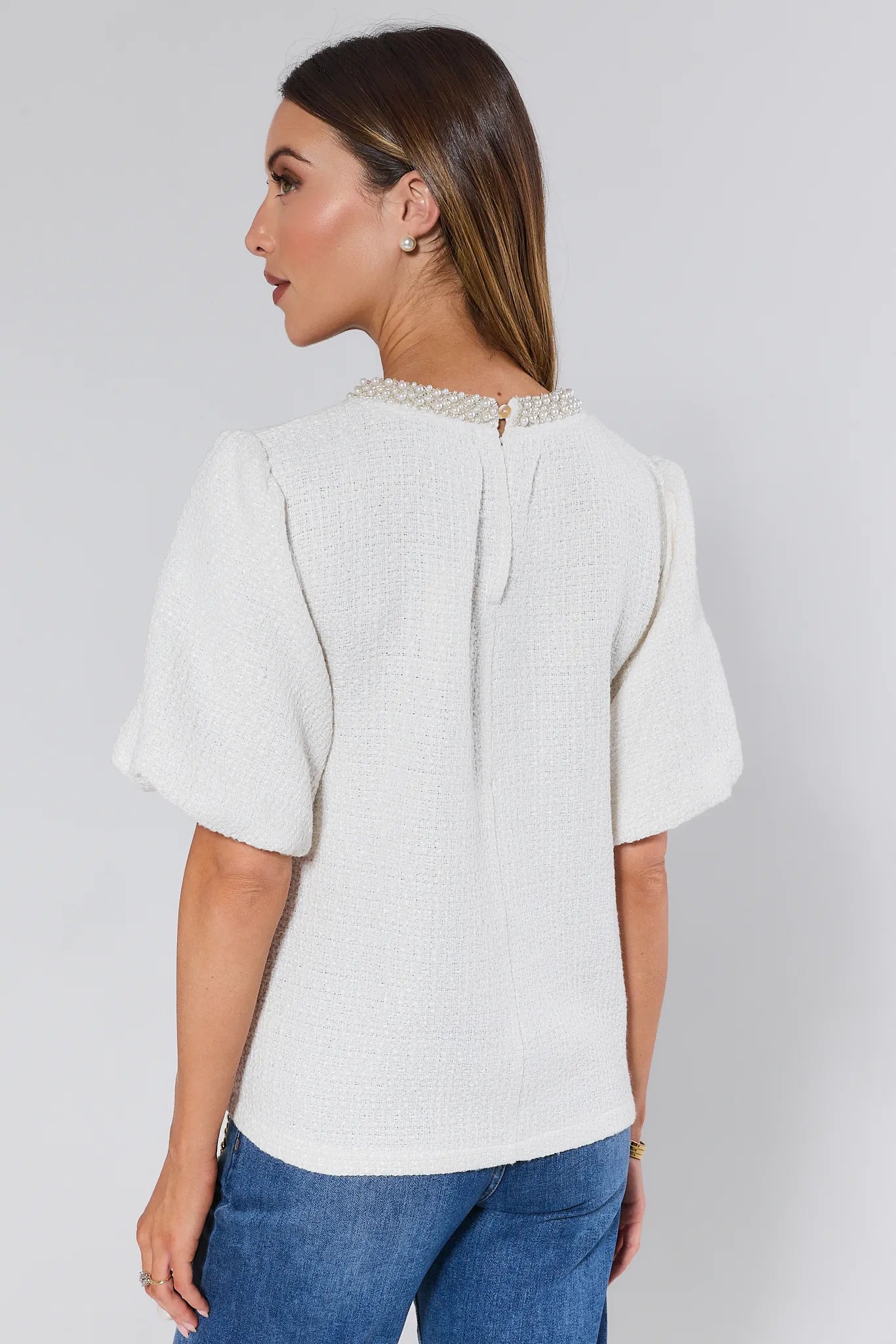 Woman wearing a white Blakely Top with pearl details against a plain