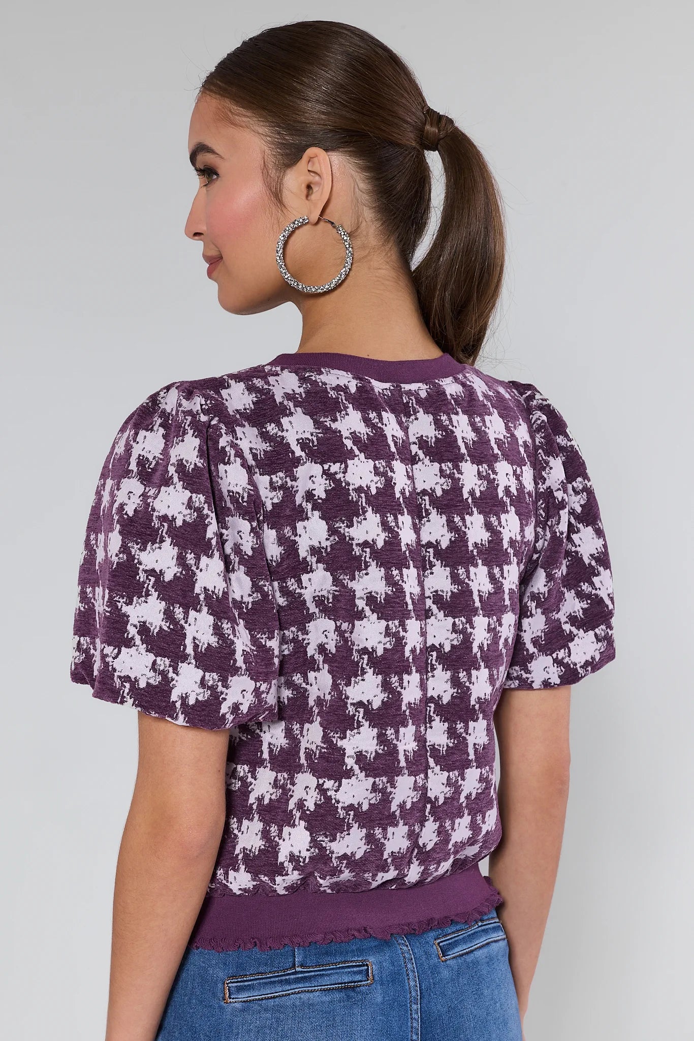 Woman wearing a purple Mason Top and white patterned top against a plain background