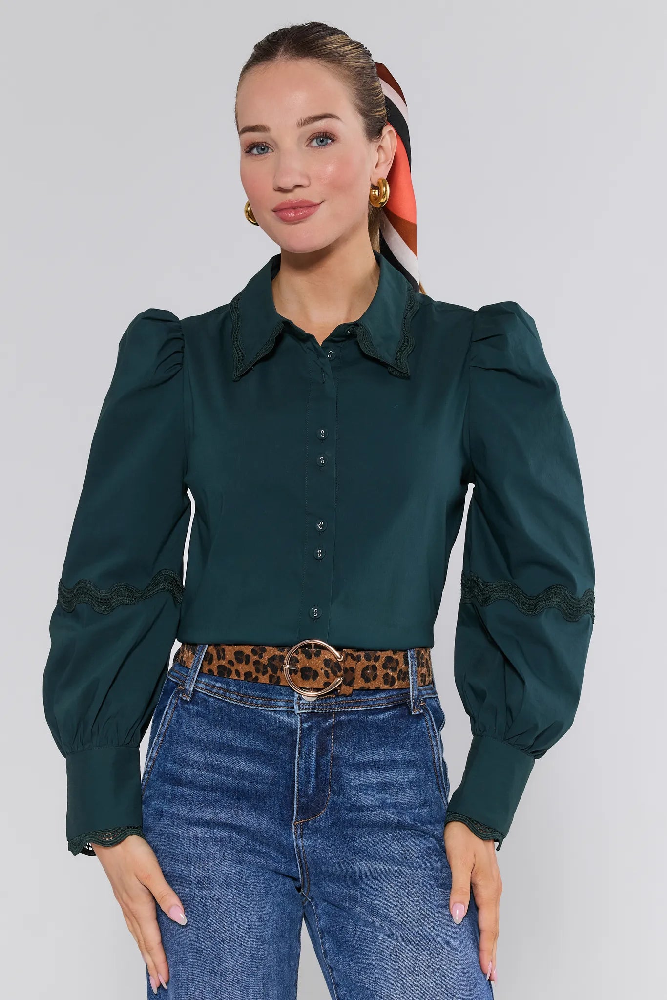 Woman wearing a dark green Ellis Top with puffed sleeves and blue jeans on a plain background
