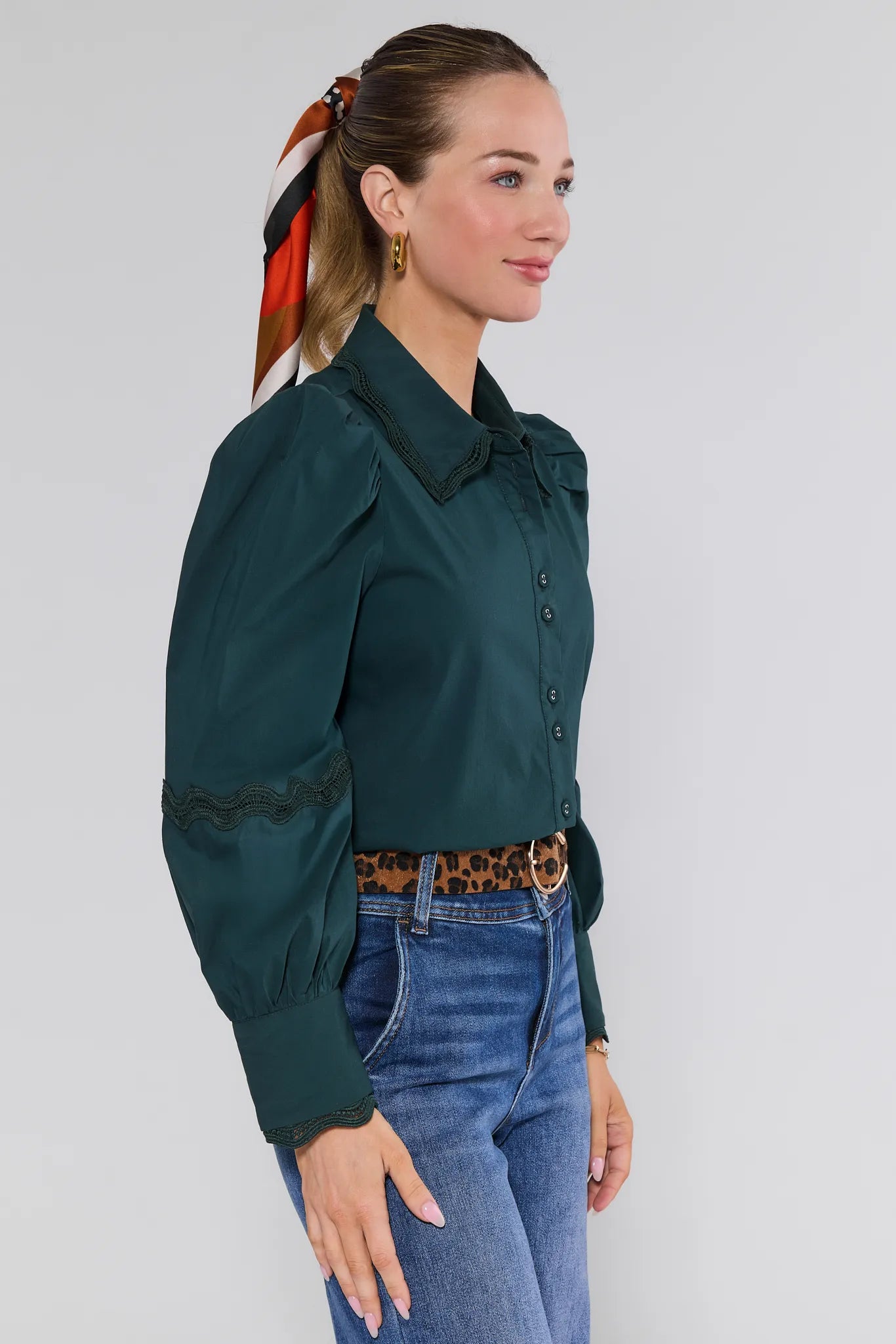 Woman wearing a dark green Ellis Top and blue jeans with a white background