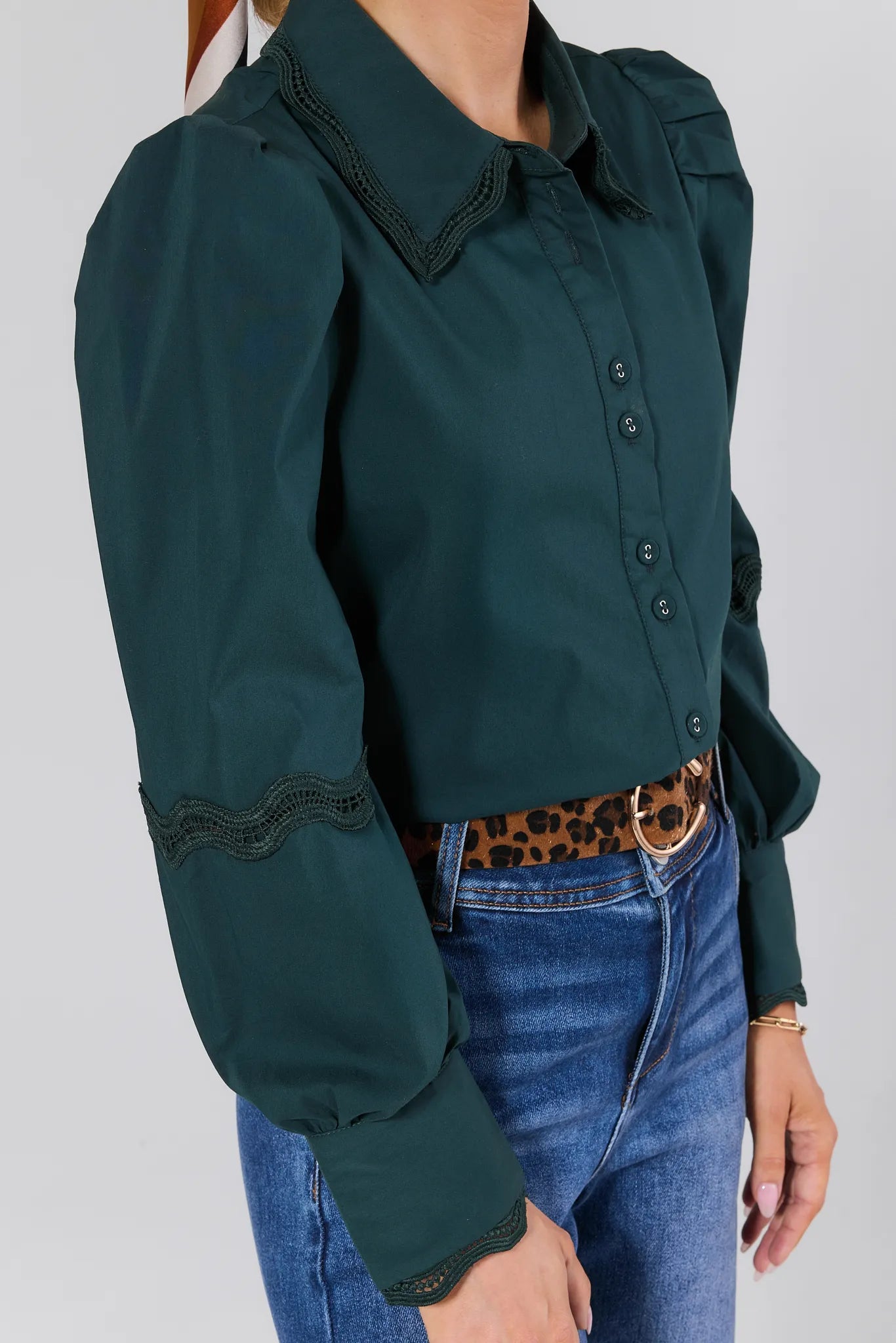 Green Ellis Top with lace details worn by a person, paired with blue jeans and a leopard print belt.