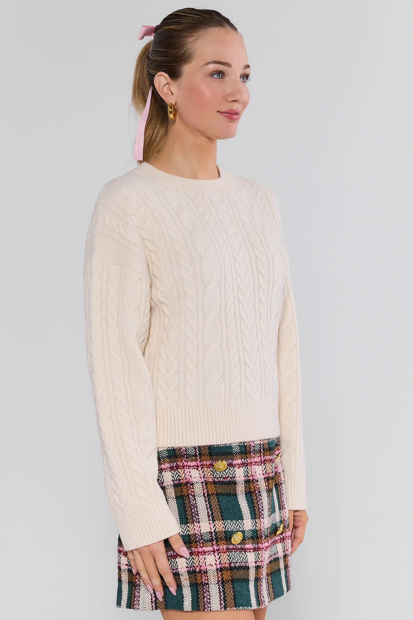 Woman wearing a cream Dakota Sweater and plaid skirt against a white background