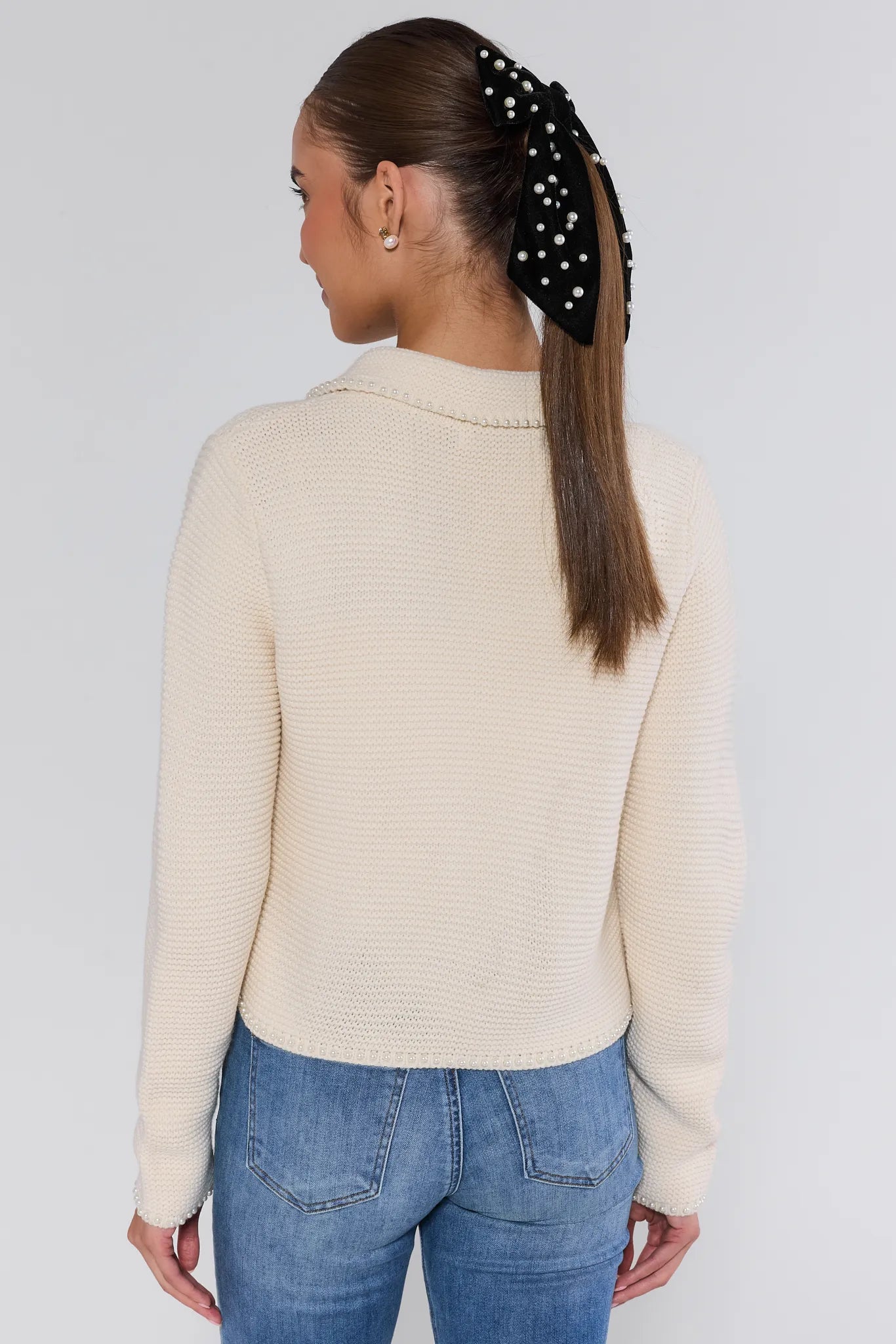 Woman wearing a cream-colored teagan cardigan and blue jeans on a plain background