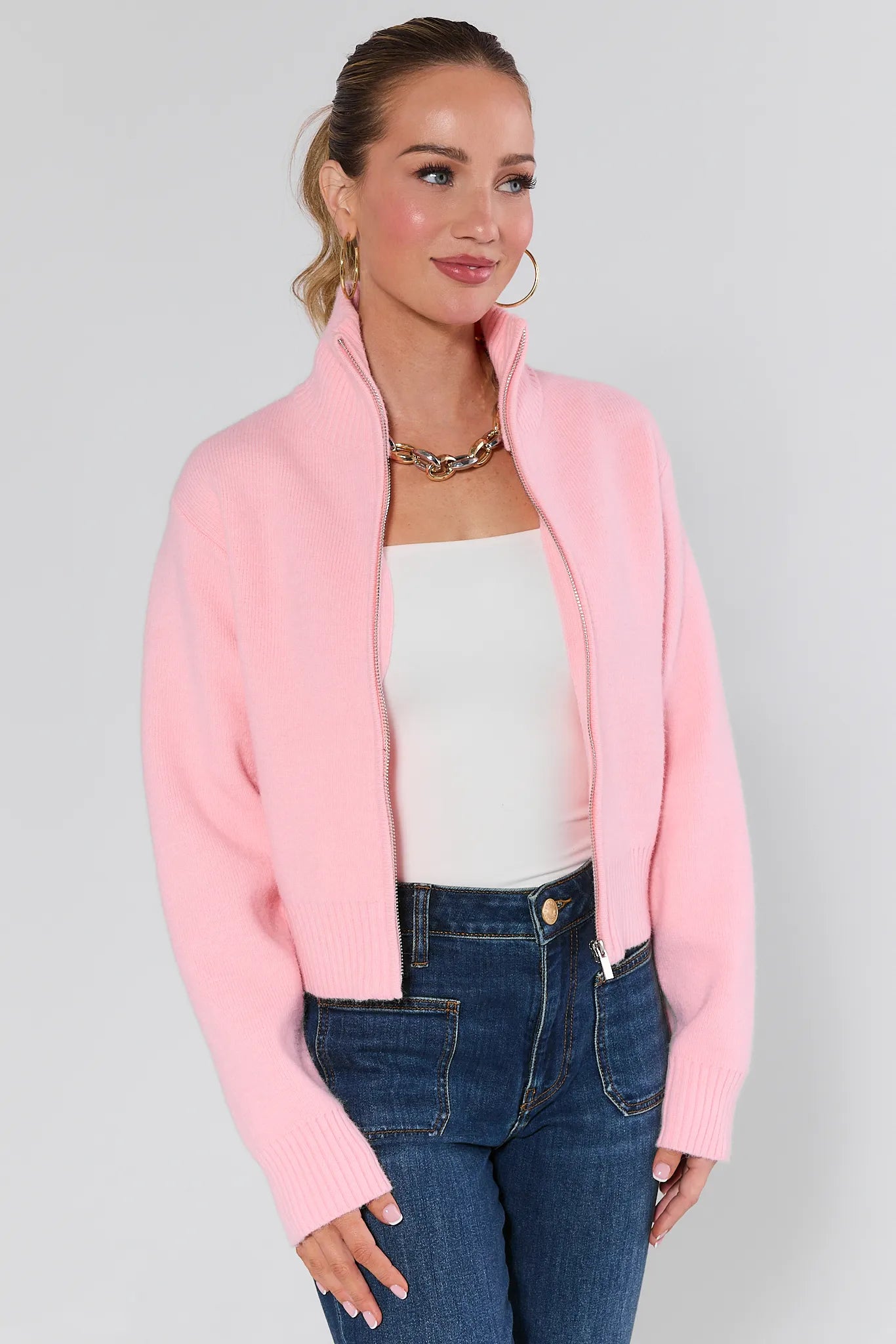 Woman wearing a Brighton Sweater over a white top and blue jeans on a plain background