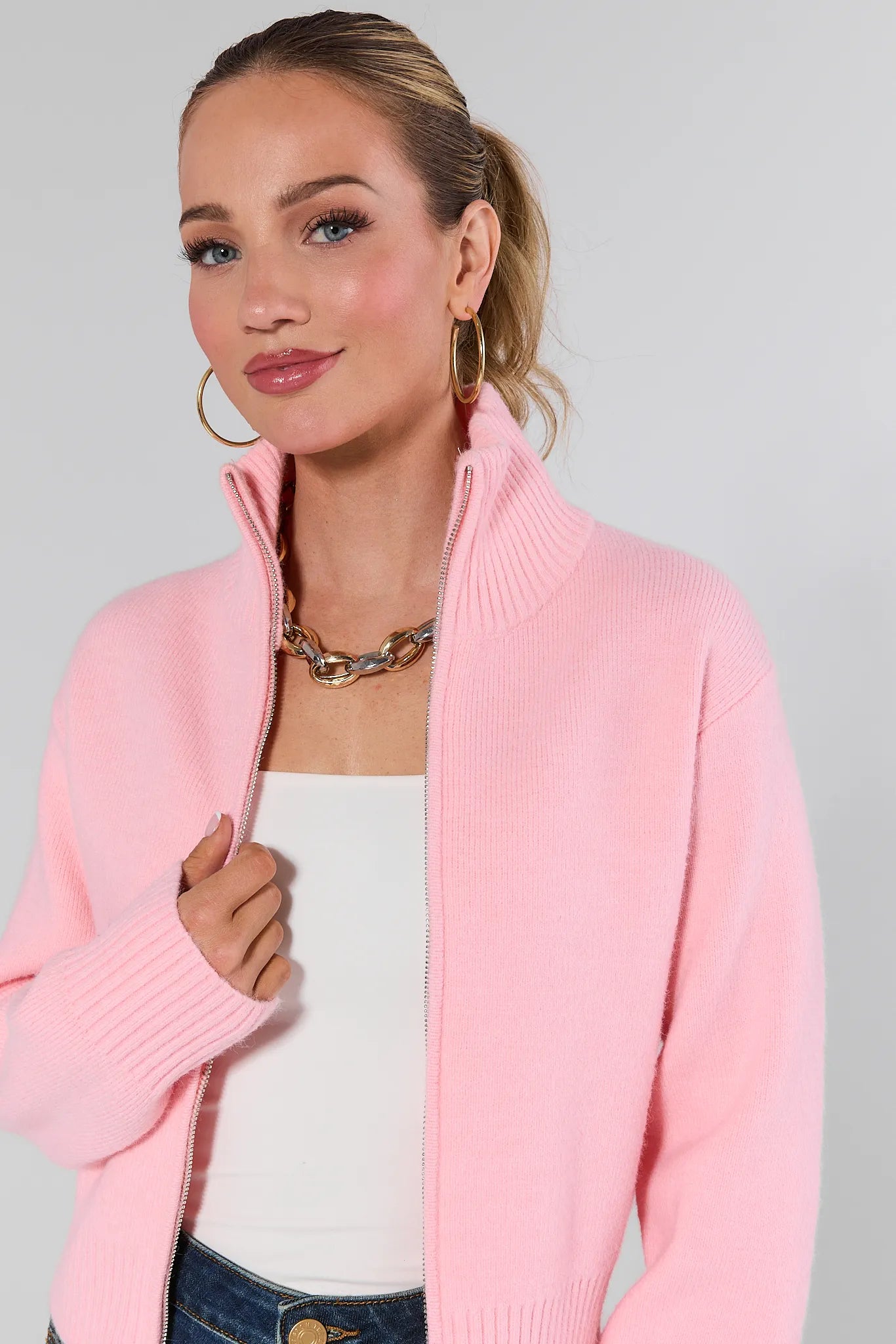 Woman wearing a Brighton Sweater over a white top and blue jeans on a plain background