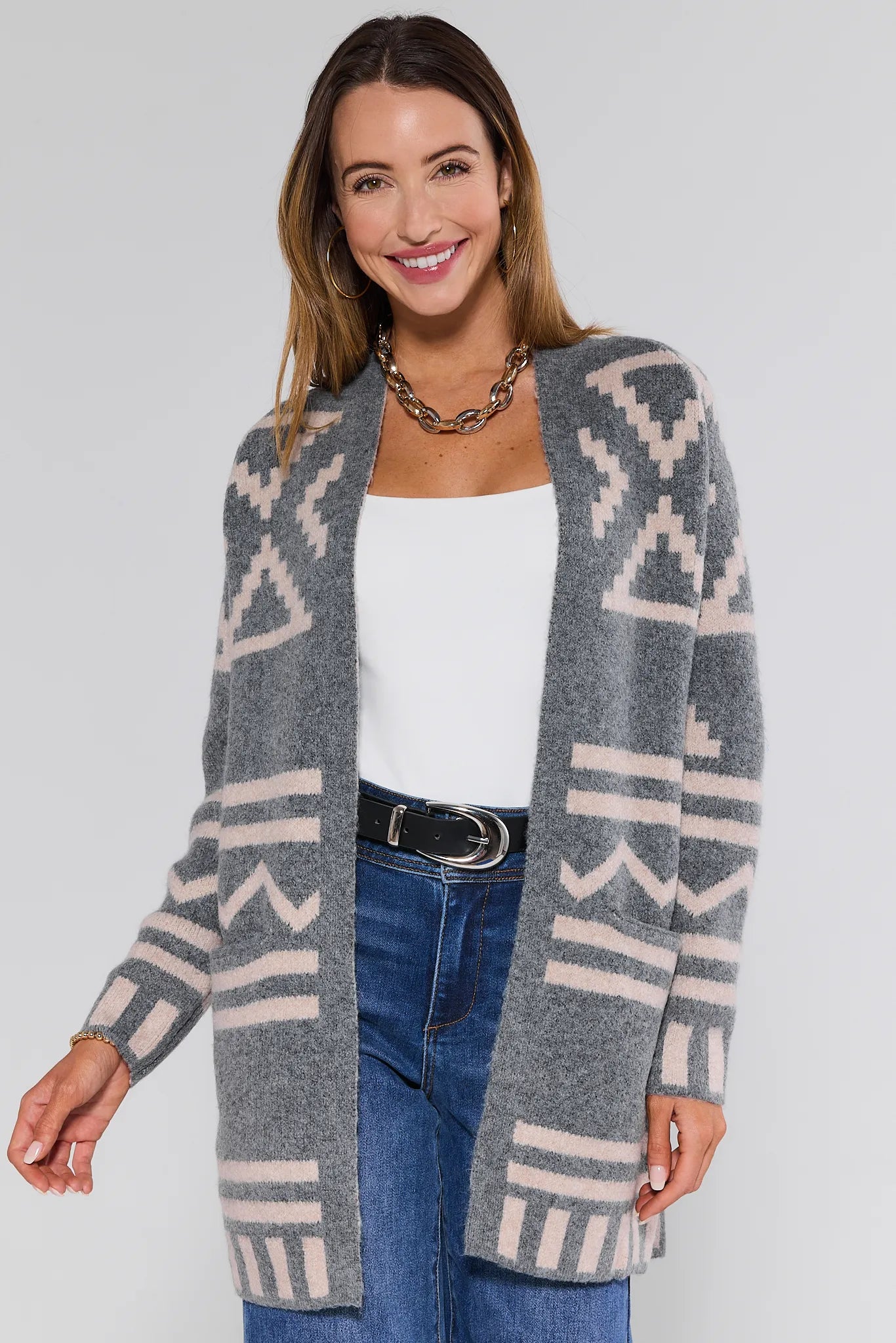 Woman wearing a patterned Helena Cardigan over a white top and blue jeans on a plain background