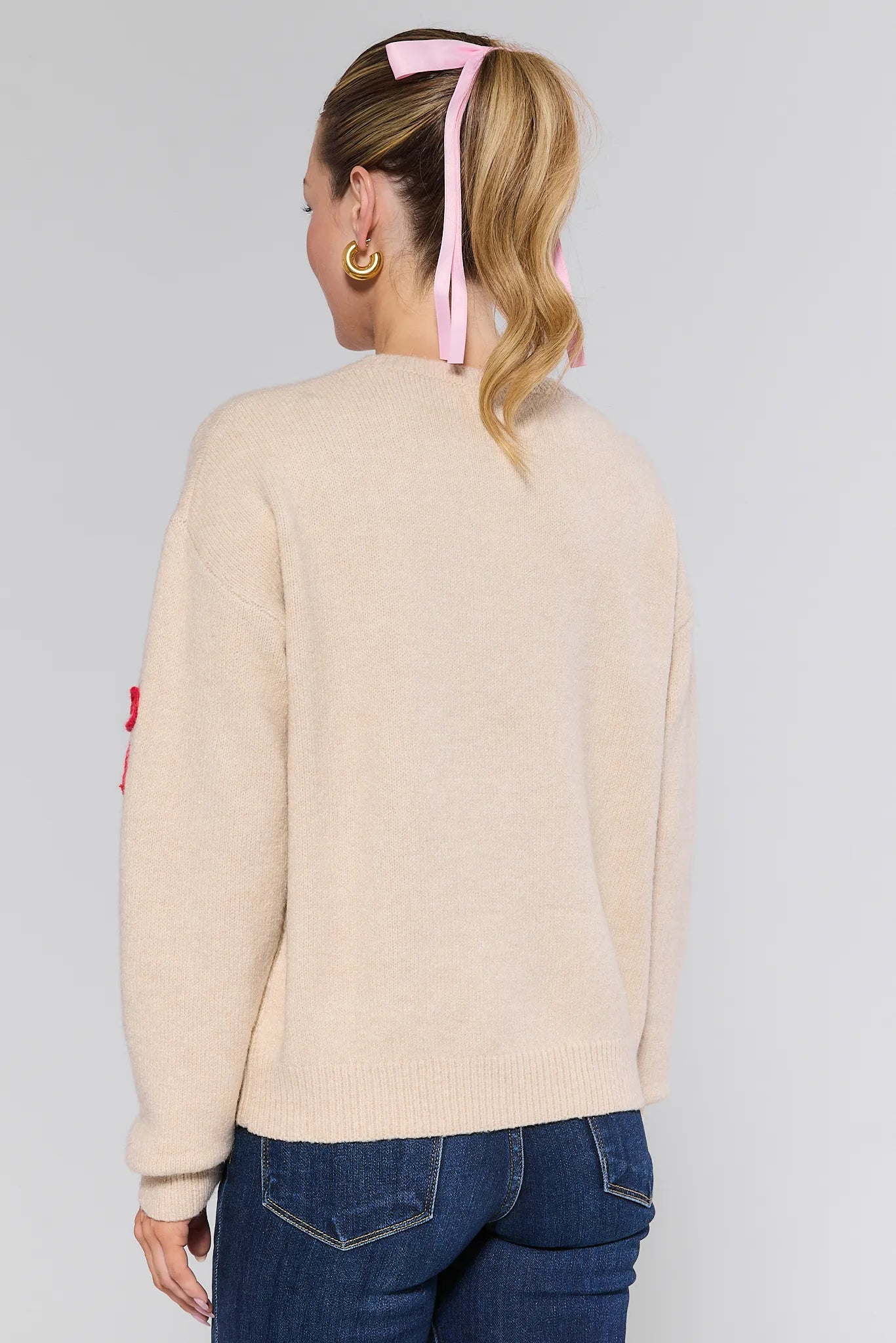 Person wearing a beige Giselle Sweater with a red detail and blue jeans on a plain background