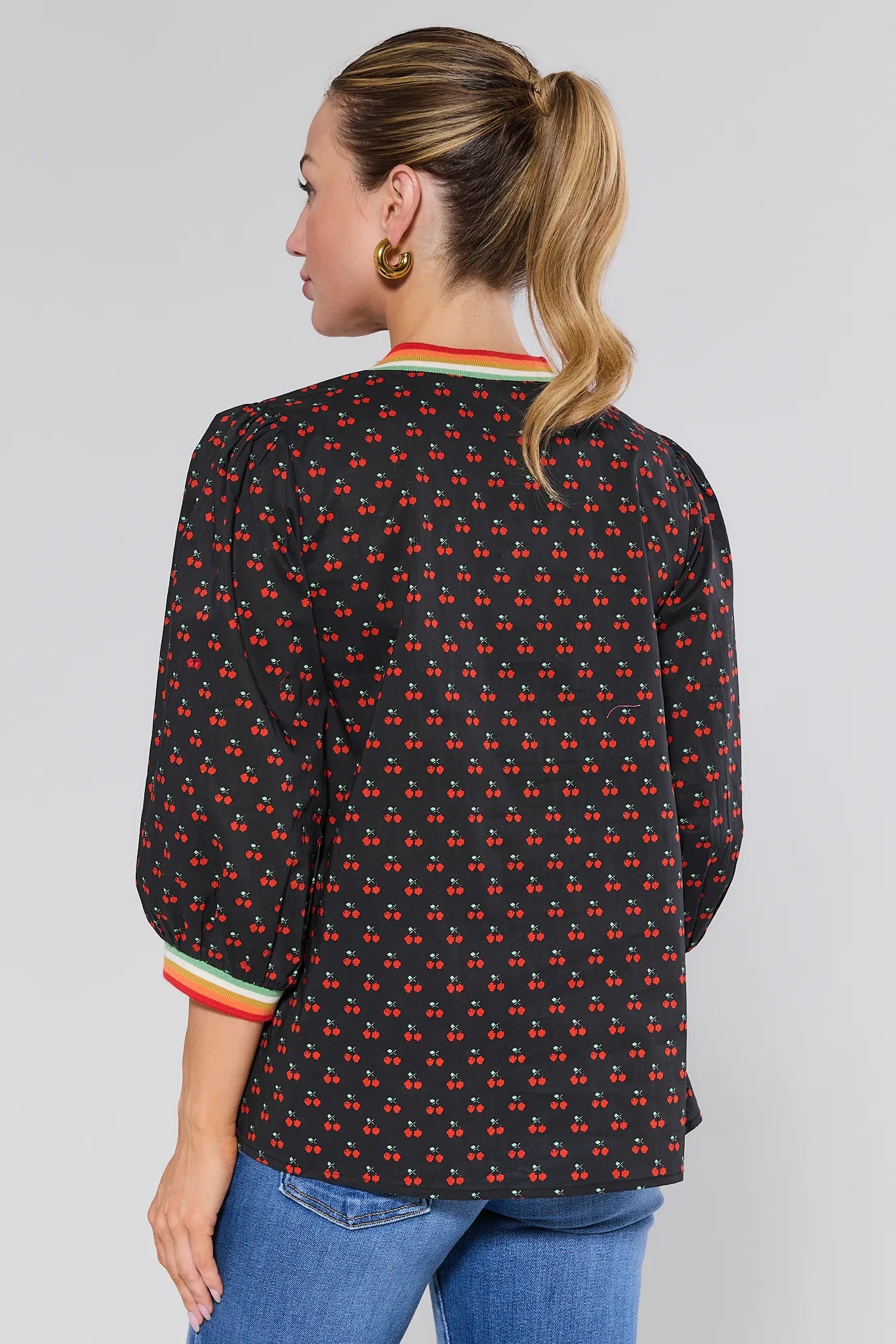 Woman wearing a black patterned Bailey Top with blue jeans on a plain background