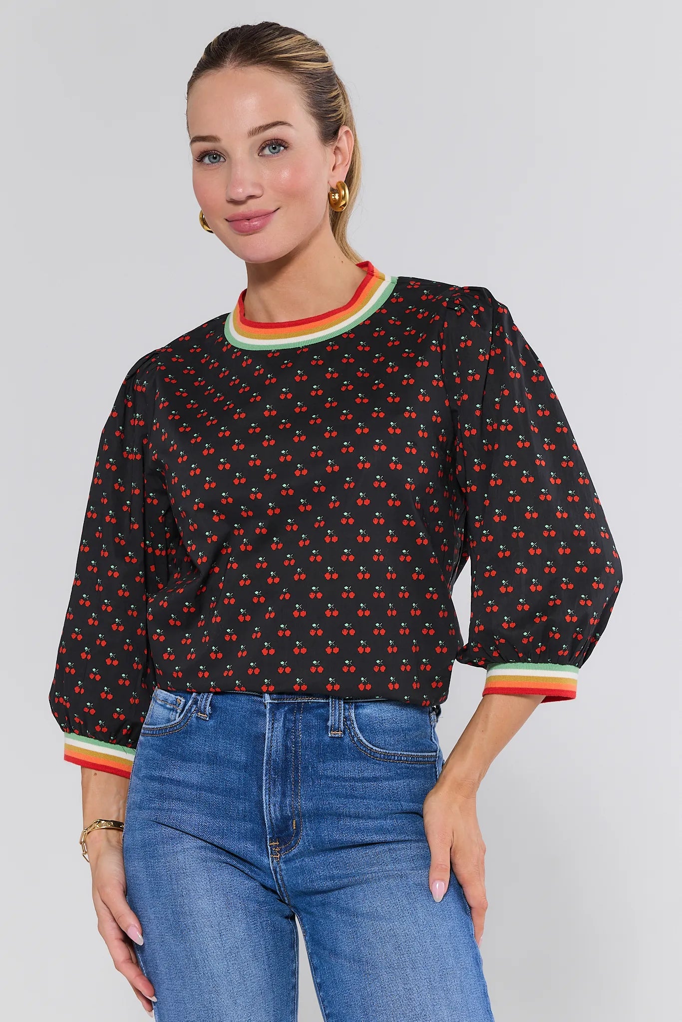 Woman wearing a black patterned Bailey Top with colorful cuffs and trim, paired with blue jeans on a white background.