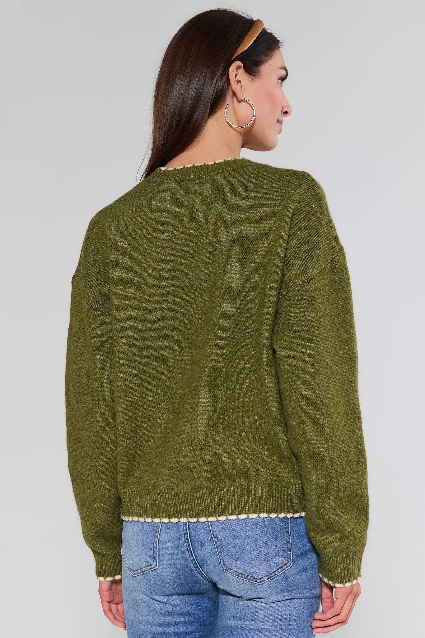 Person wearing a olive Lottie Sweater and blue jeans on a white background