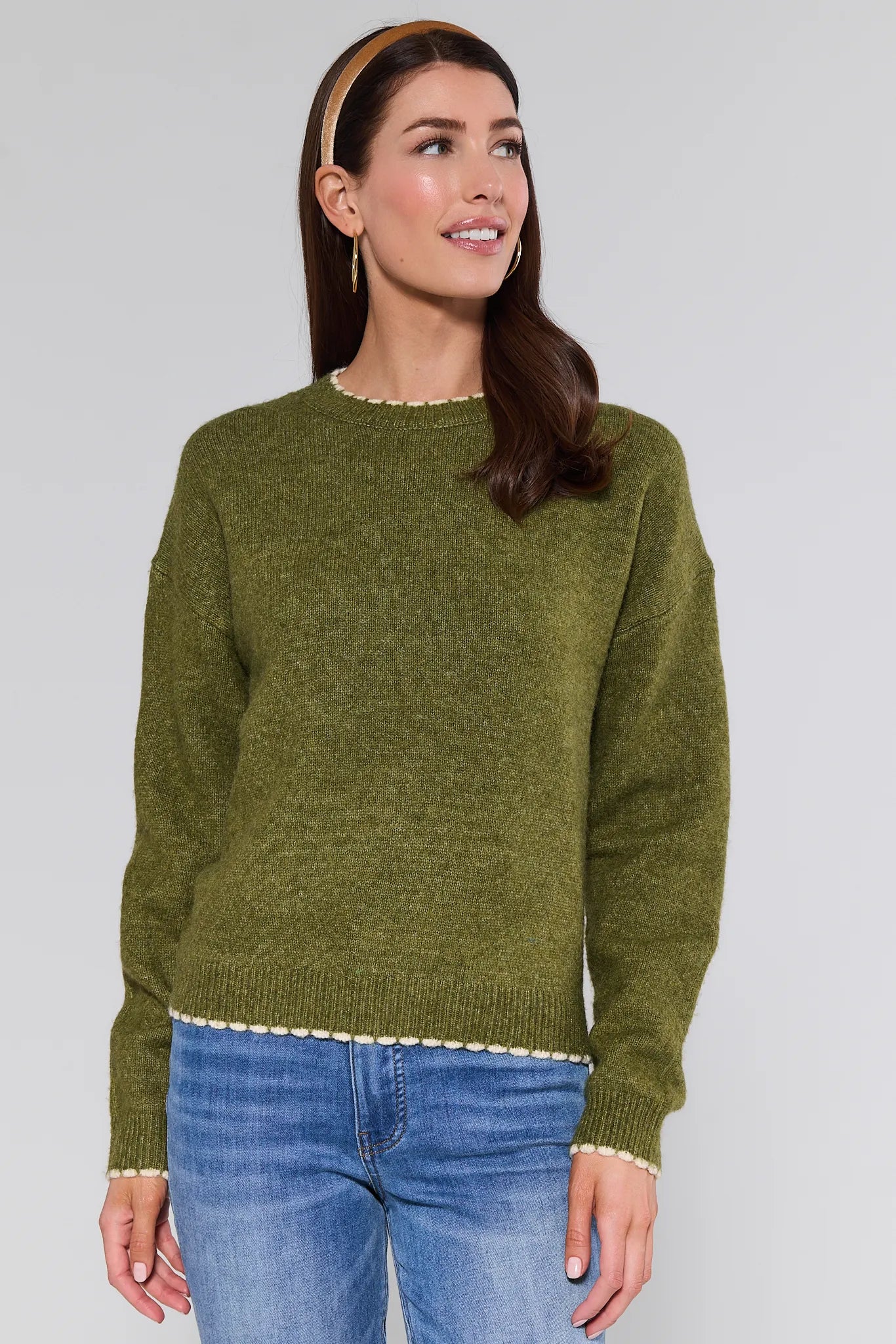 Woman wearing a olive Lottie Sweater and blue jeans against a plain background