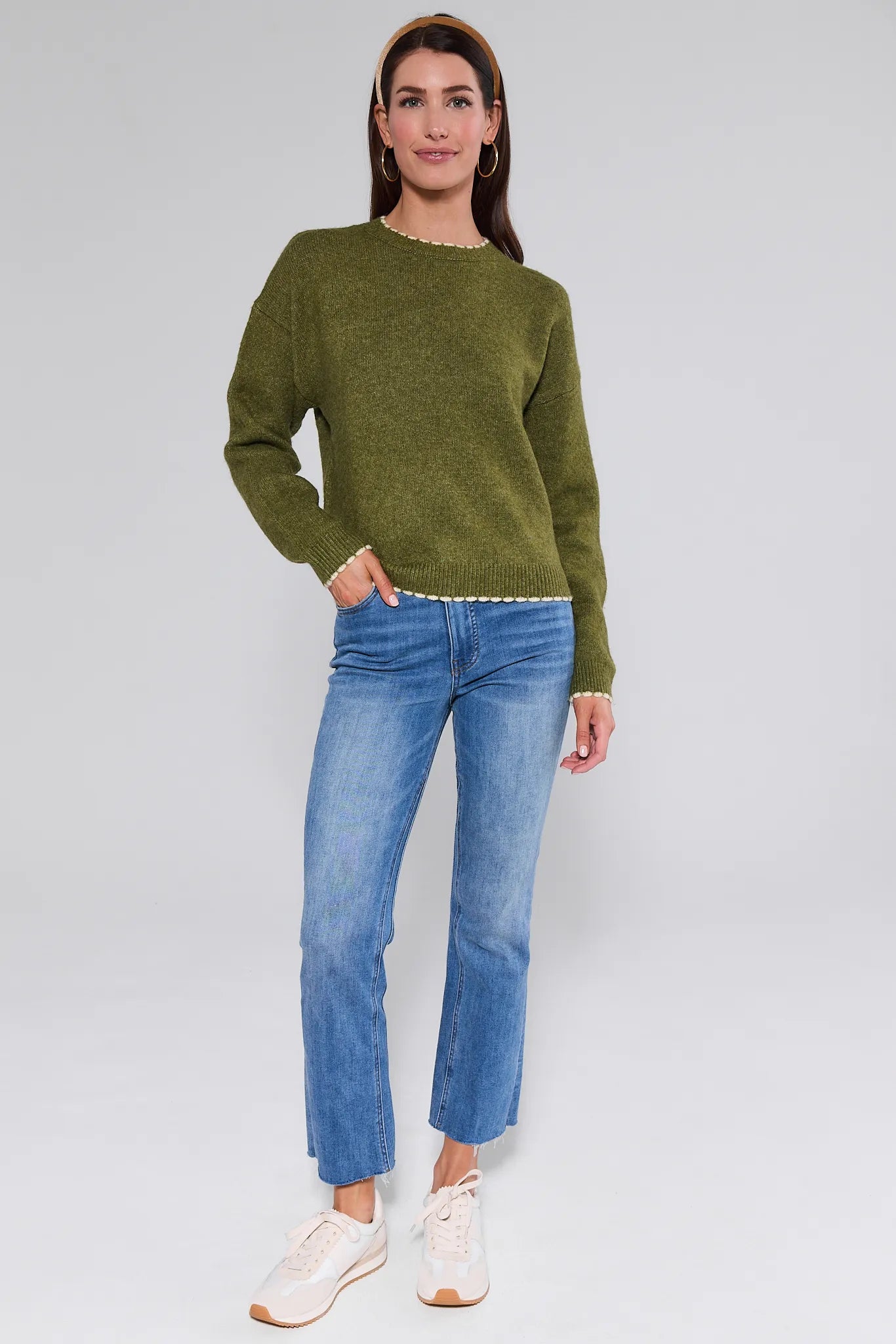Woman wearing a olive Lottie Sweater and blue jeans on a white background