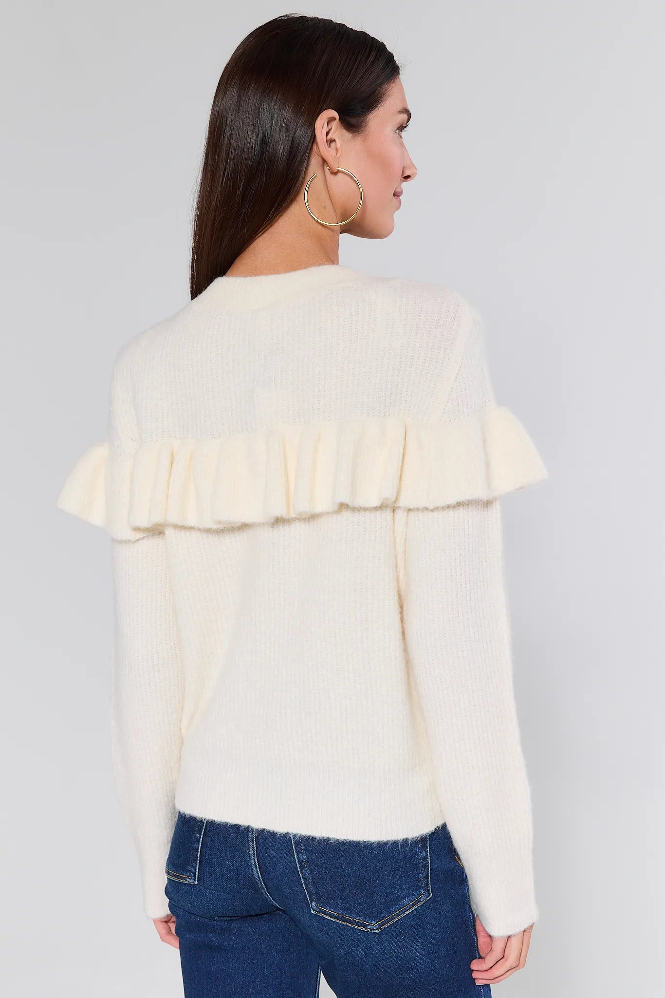 Woman wearing a Demi Ivory Ruffle Cardigan with ruffled sleeves and blue jeans on a white background