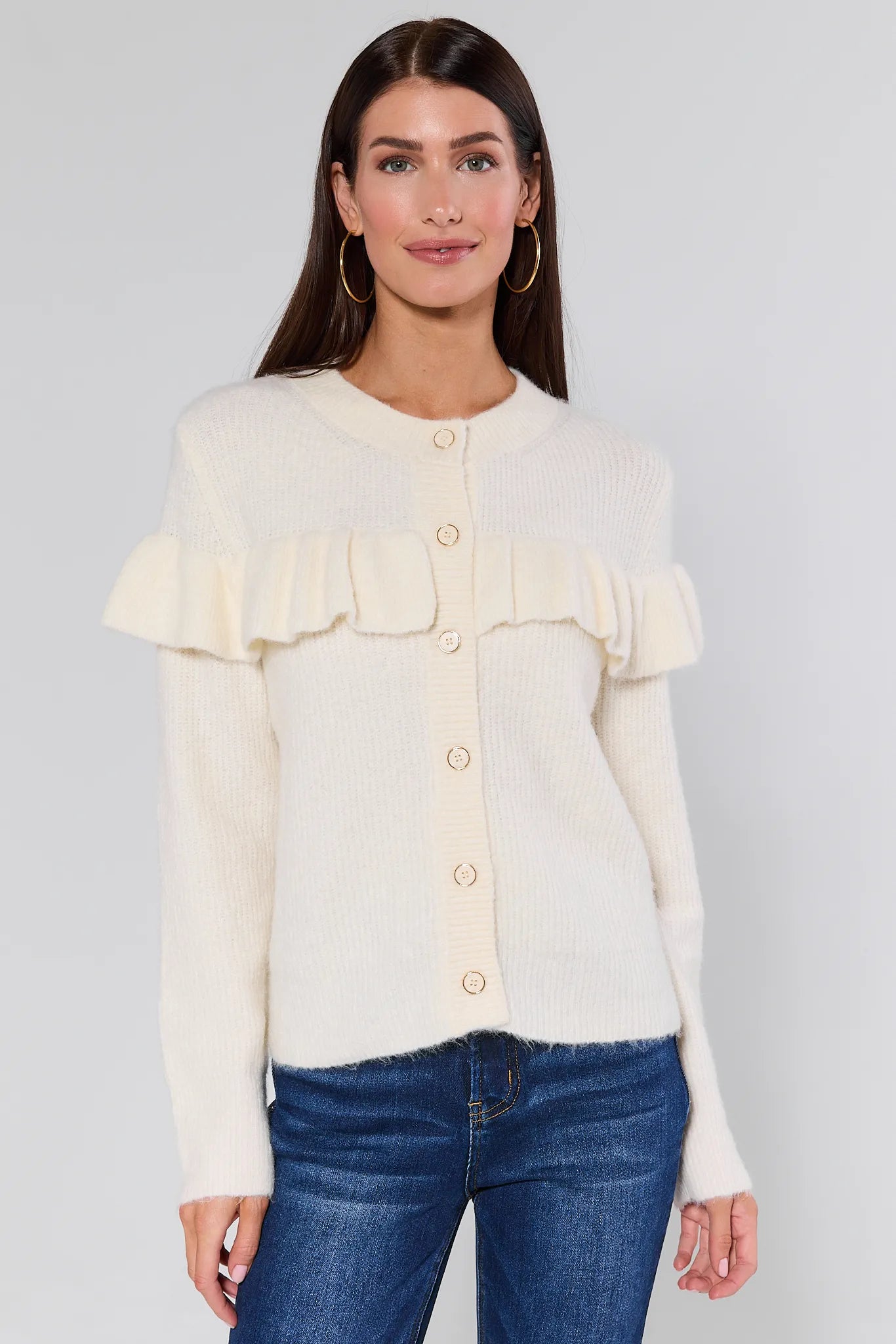 Woman wearing a Demi Ivory Ruffle Cardigan with ruffled sleeves and blue jeans on a white background