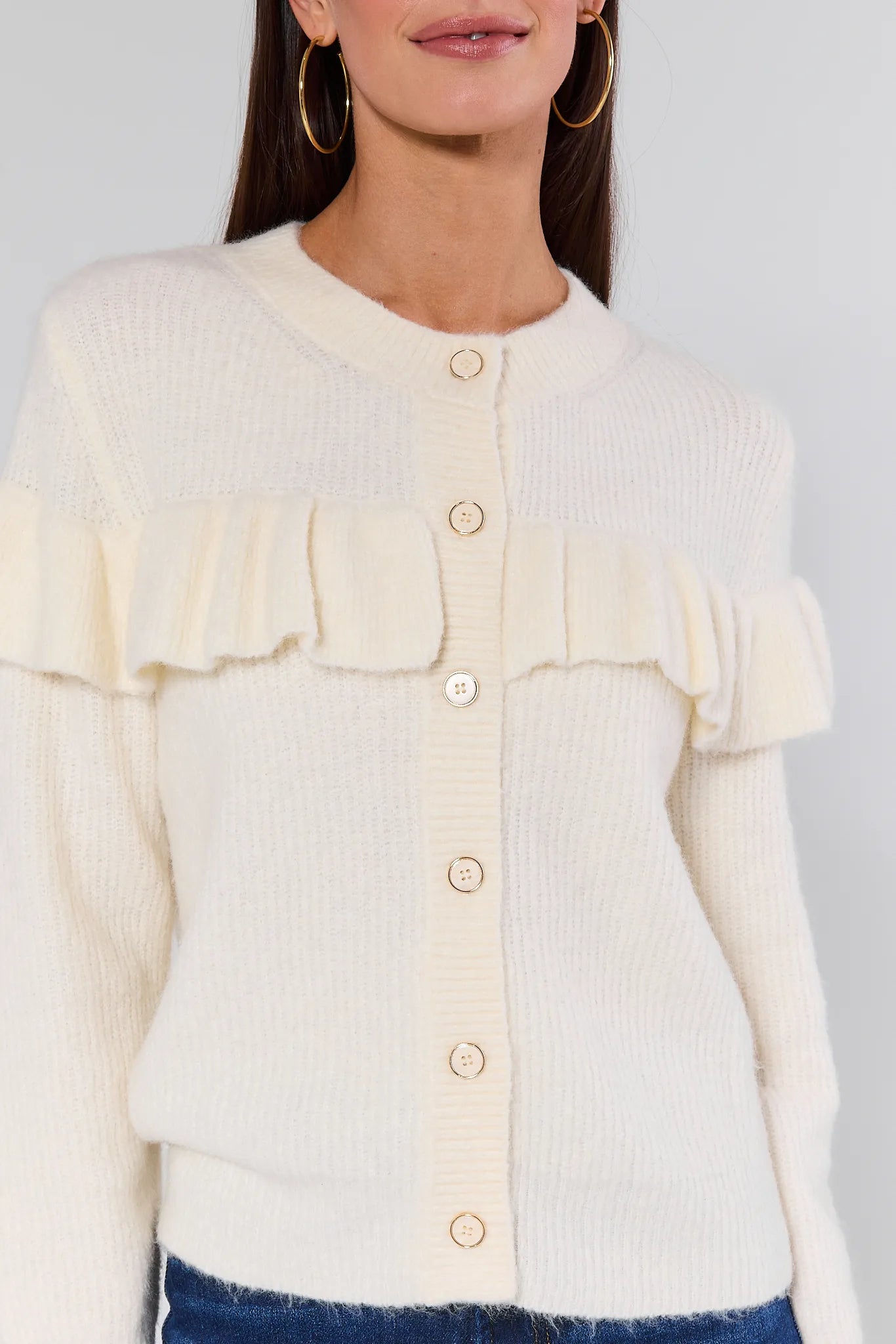 Woman wearing a Demi Ivory Ruffle Cardigan with ruffled sleeves and blue jeans on a white background
