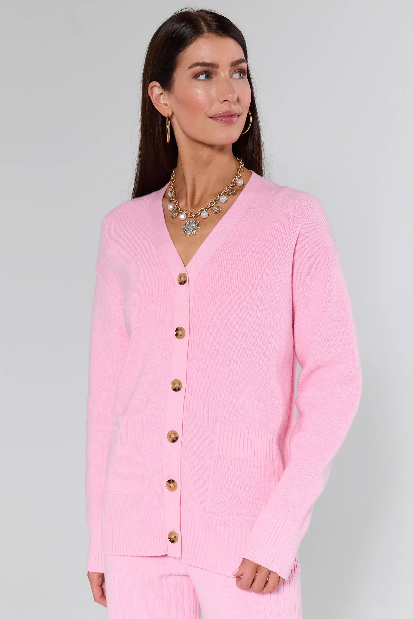 Woman wearing a Brianna Pink Knit Cardigan with gold buttons on a gray background