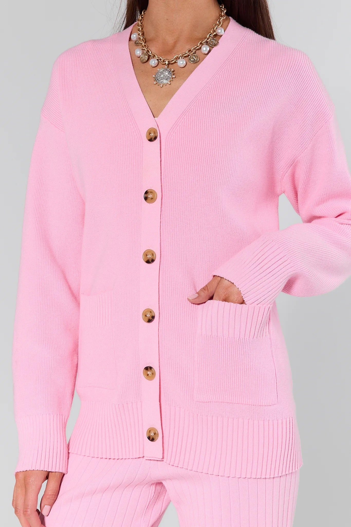 Woman wearing a Brianna Pink Knit Cardigan with gold buttons on a gray background