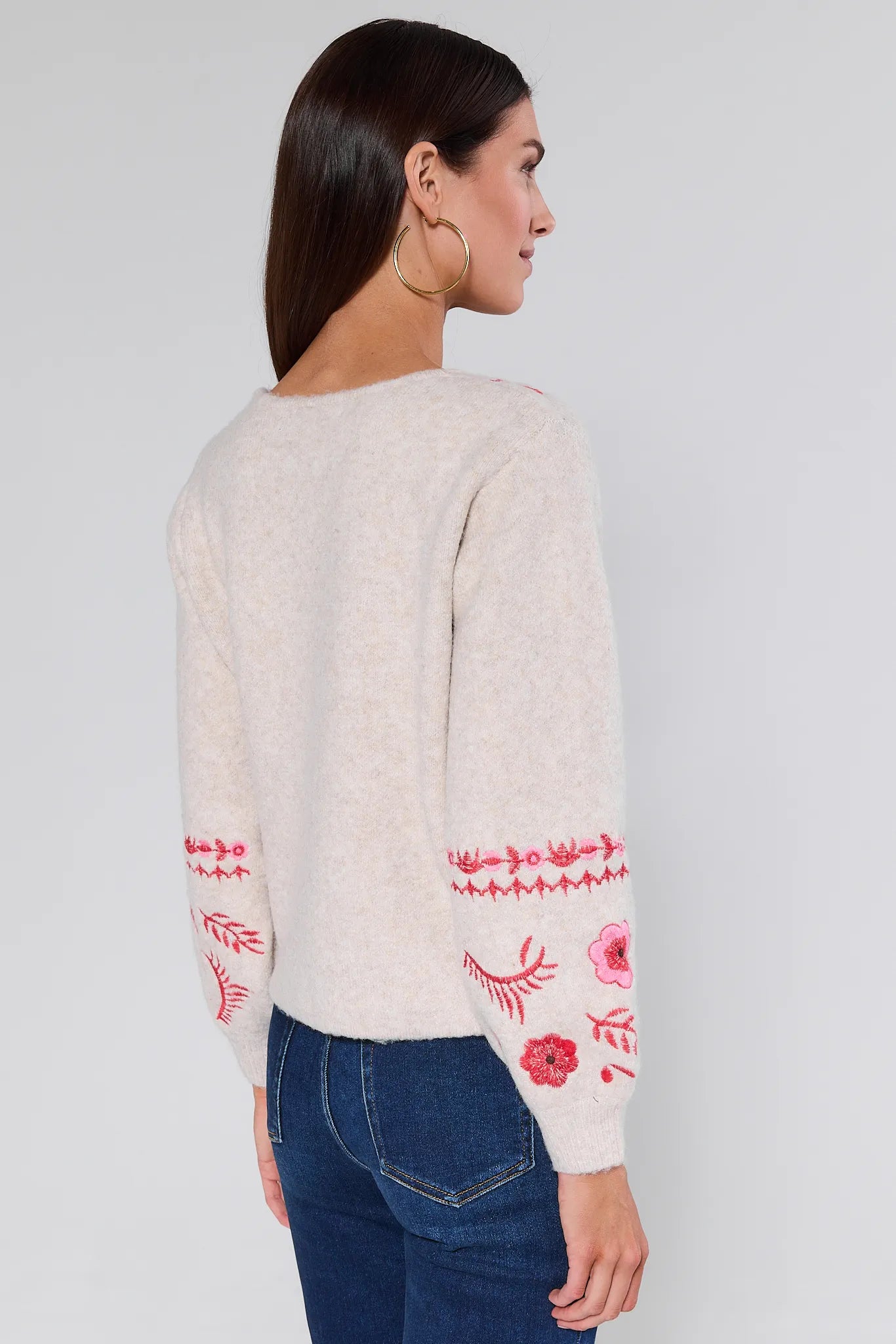 Woman wearing a Hallie Embroidered Knit Cardigan with red floral patterns on a plain background