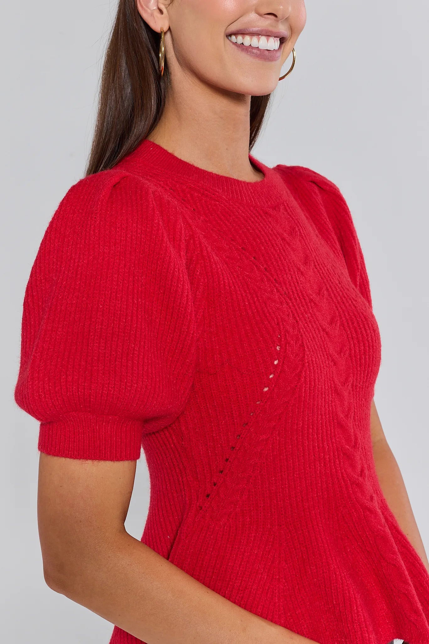 Woman wearing a red hillary sweater with puff sleeves against a plain background