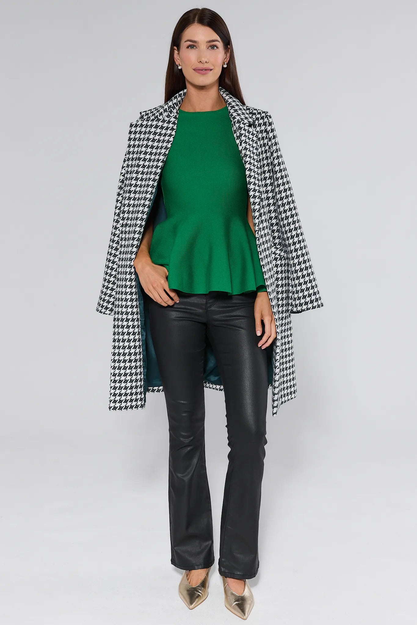 Woman wearing a houndstooth coat, green top, and black pants on a white background