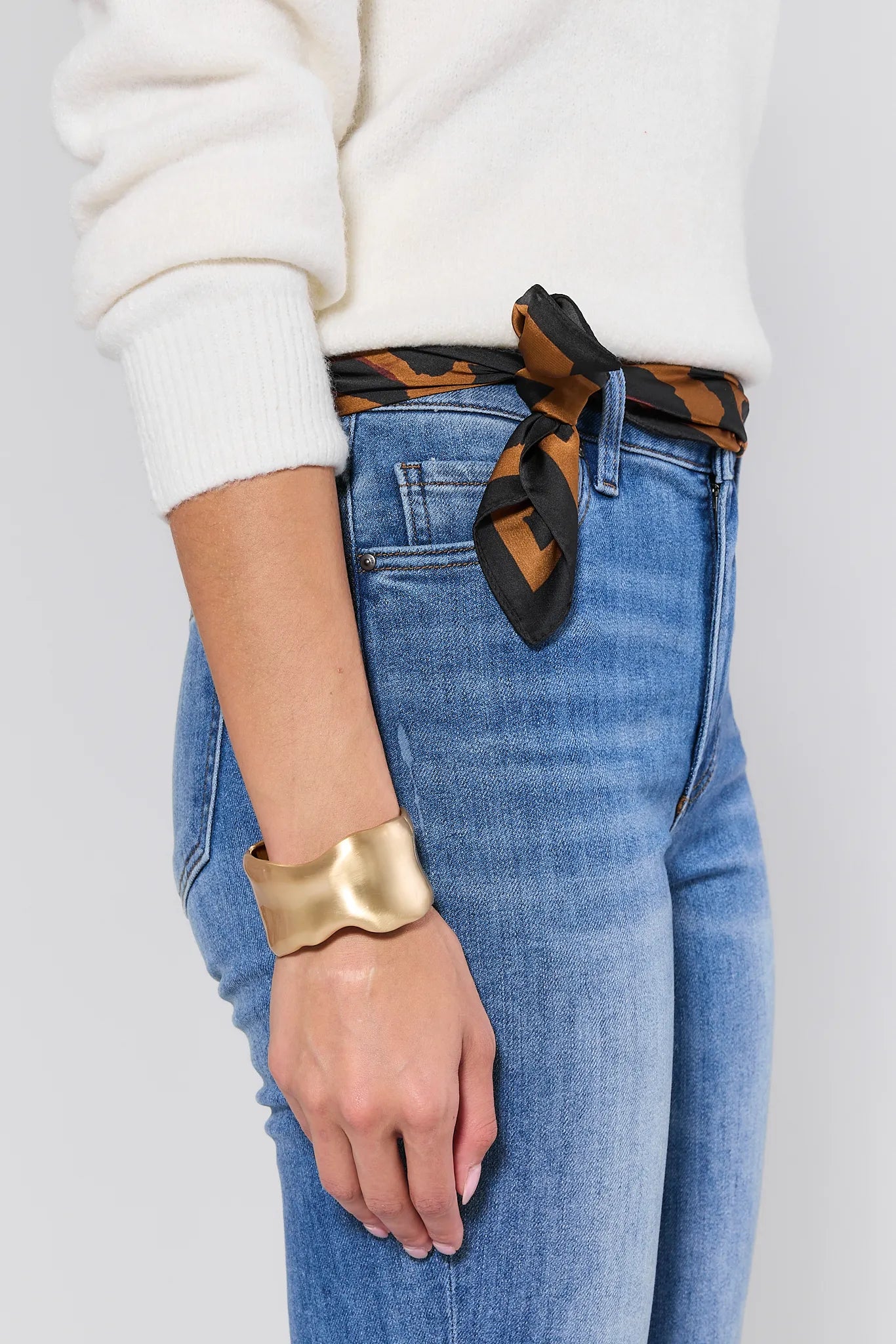 Person wearing blue jeans with a gold Arden Bracelet on a plain background