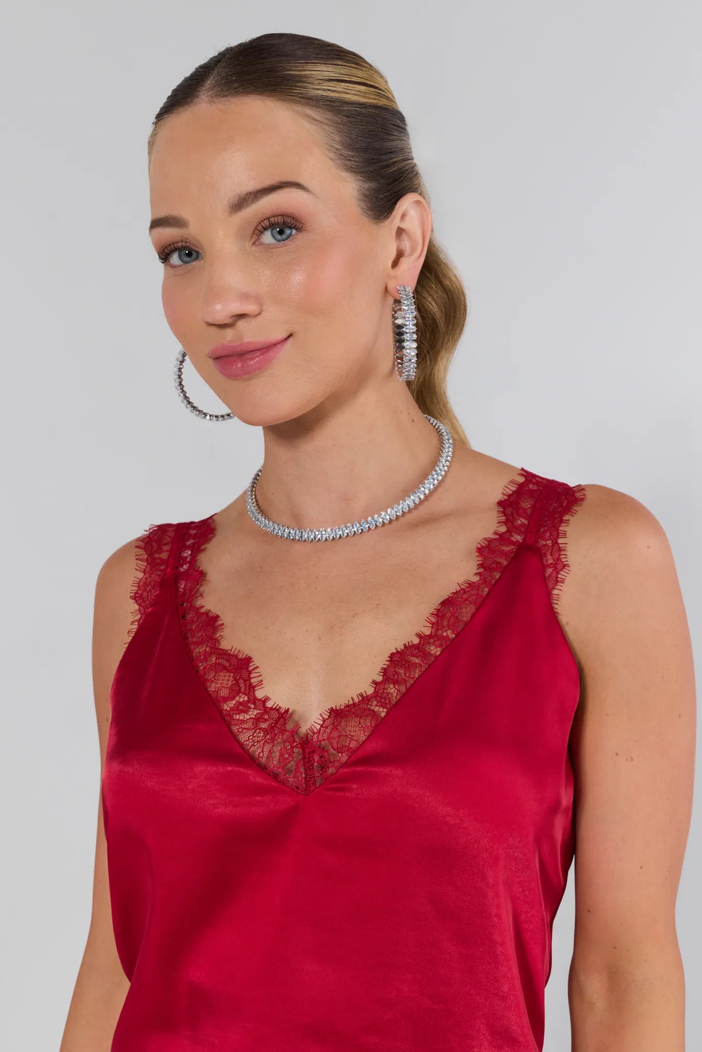Woman wearing a red dress with lace details, silver jewelry, and earrings on a plain background