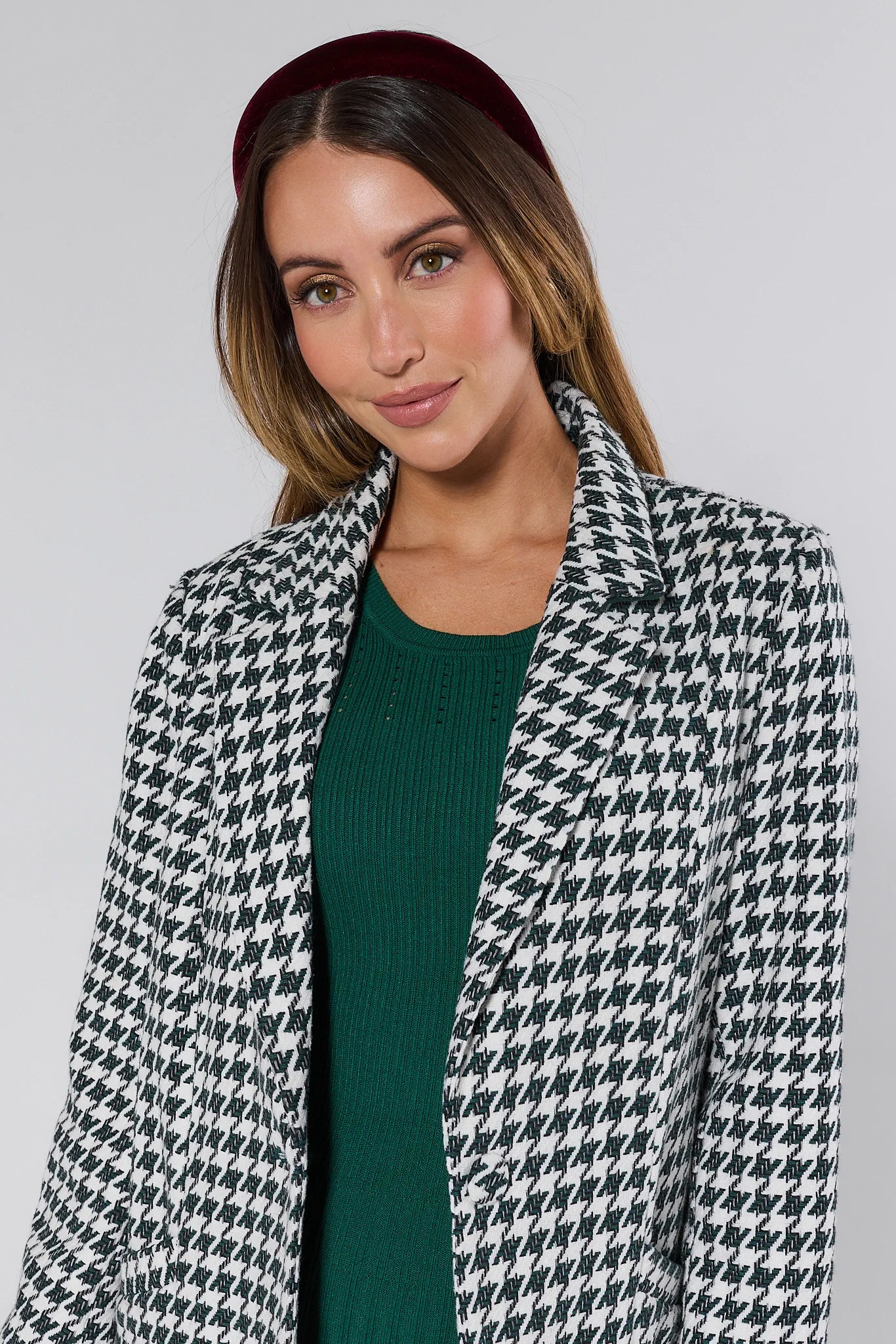 Woman wearing a Jonah Green Houndstooth Coat over a green dress with a plain background