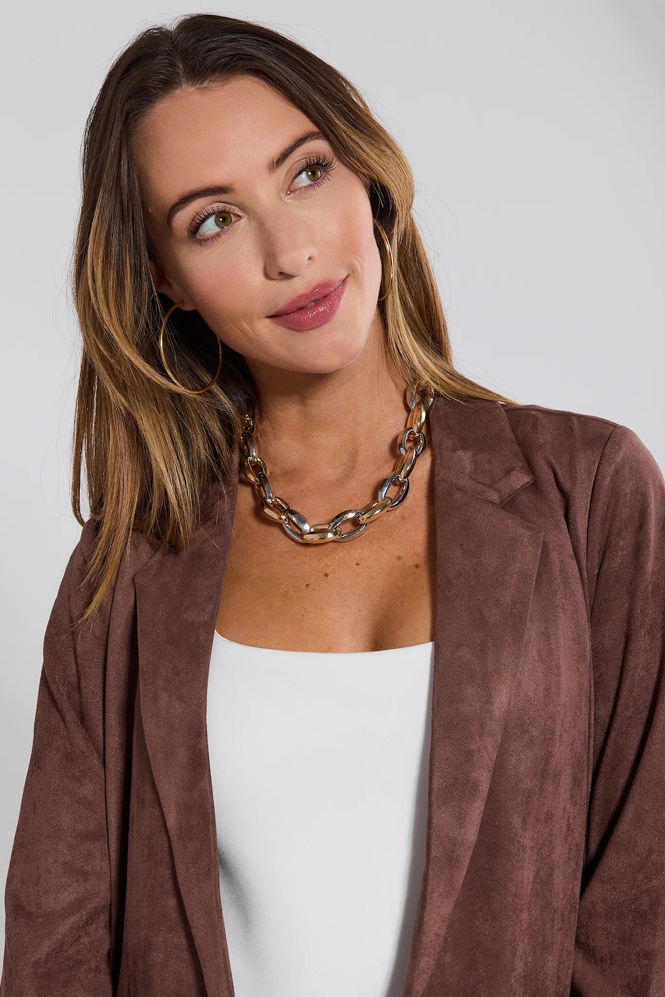 Woman wearing a brown suede Nadine Coat and white top against a plain background