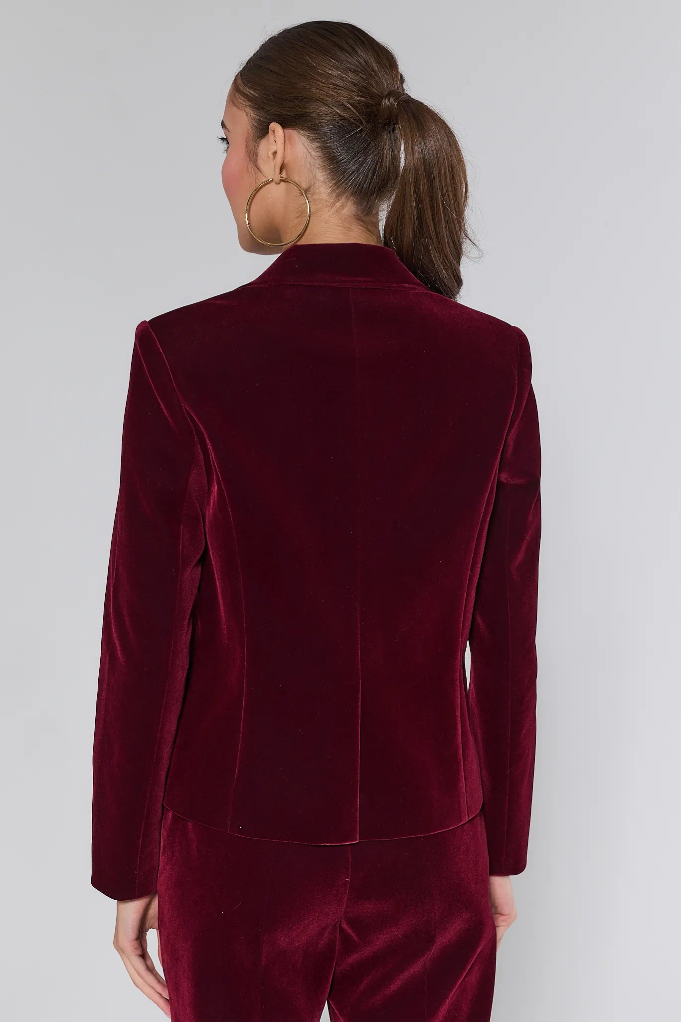 Woman wearing a Evie Canberry velvet suit with a white lace top on a plain background