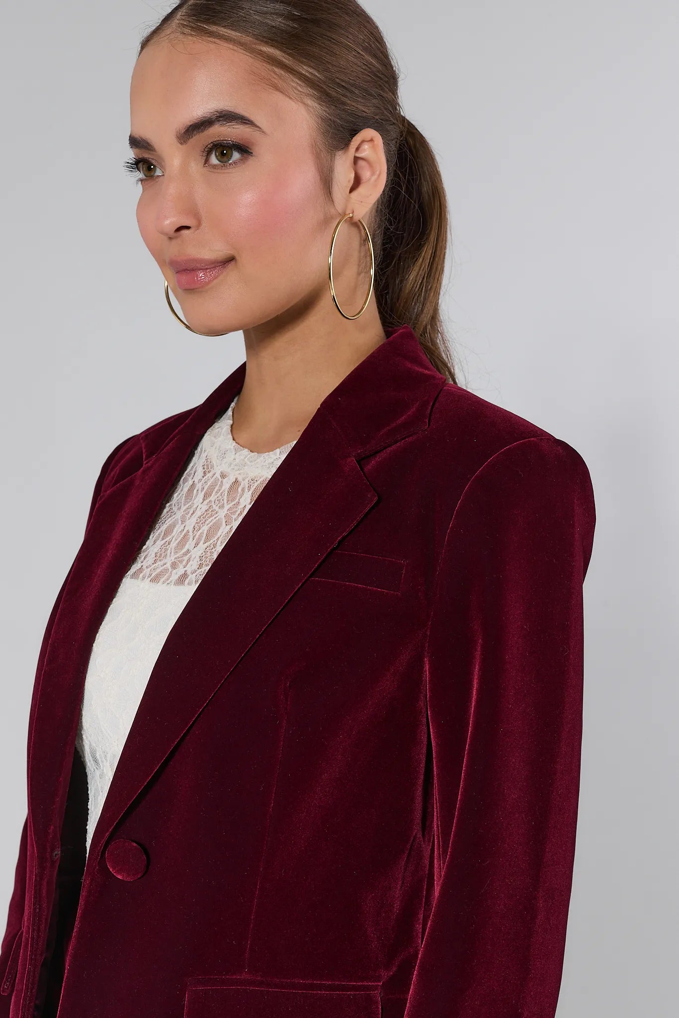 Woman wearing a Evie Canberry velvet suit with a white lace top on a plain background