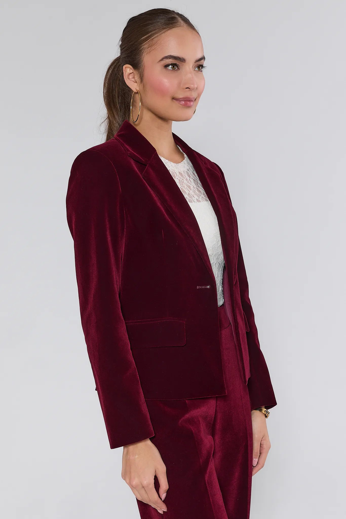 Woman wearing a Evie Canberry velvet suit with a white lace top on a plain background